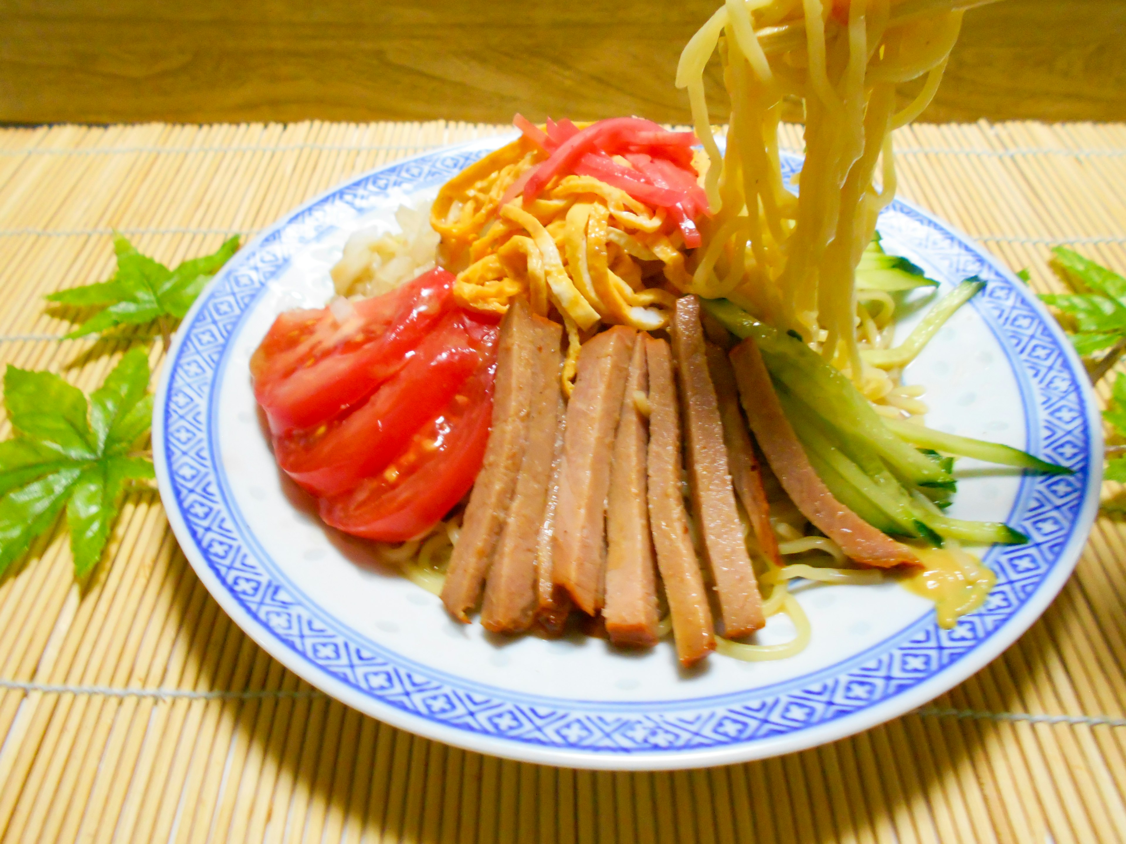 Colorful plate of cold Chinese noodles topped with sliced tomatoes and vegetables