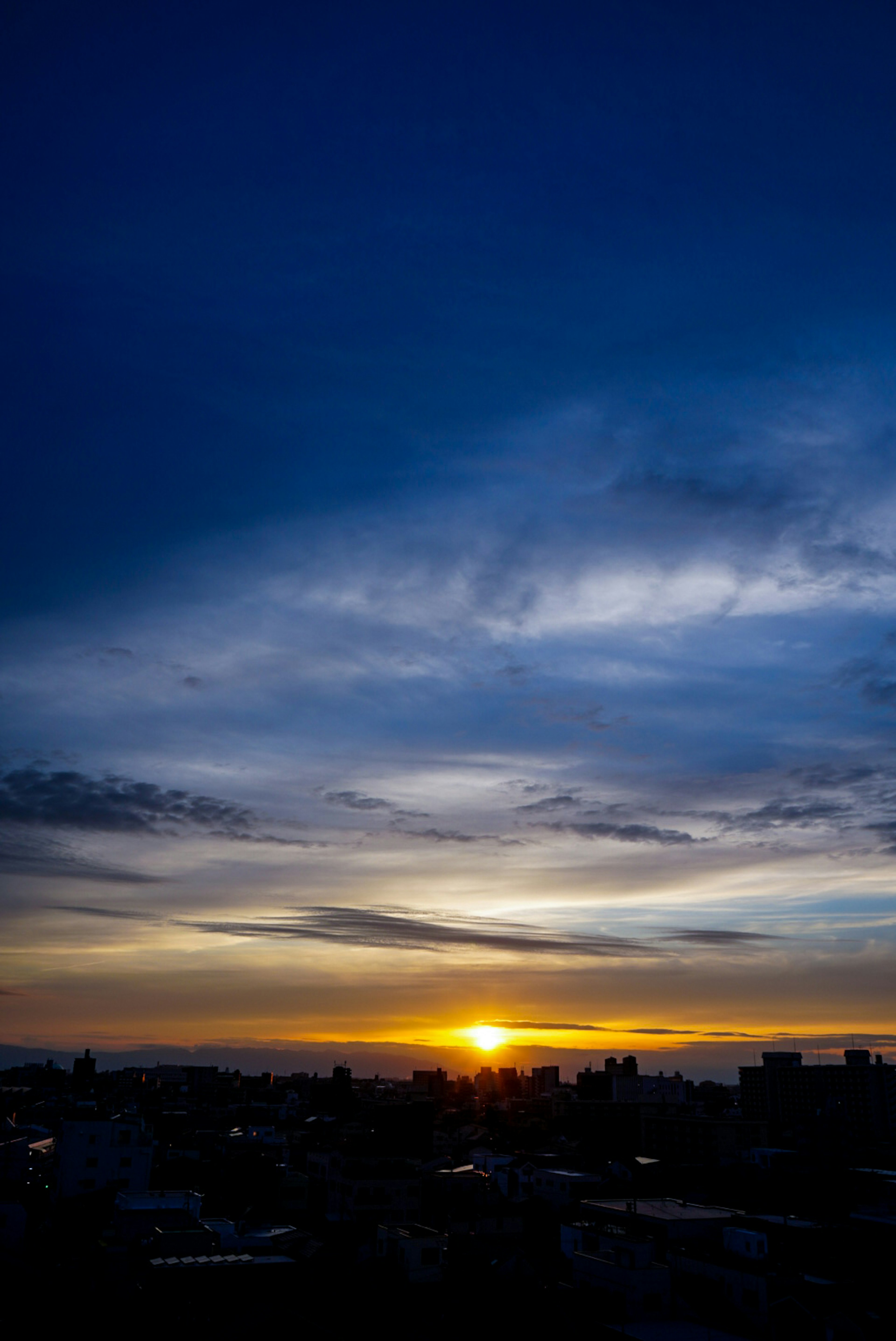 夕日が沈む美しい風景 藍色の空と雲が広がり シルエットの都市が見える