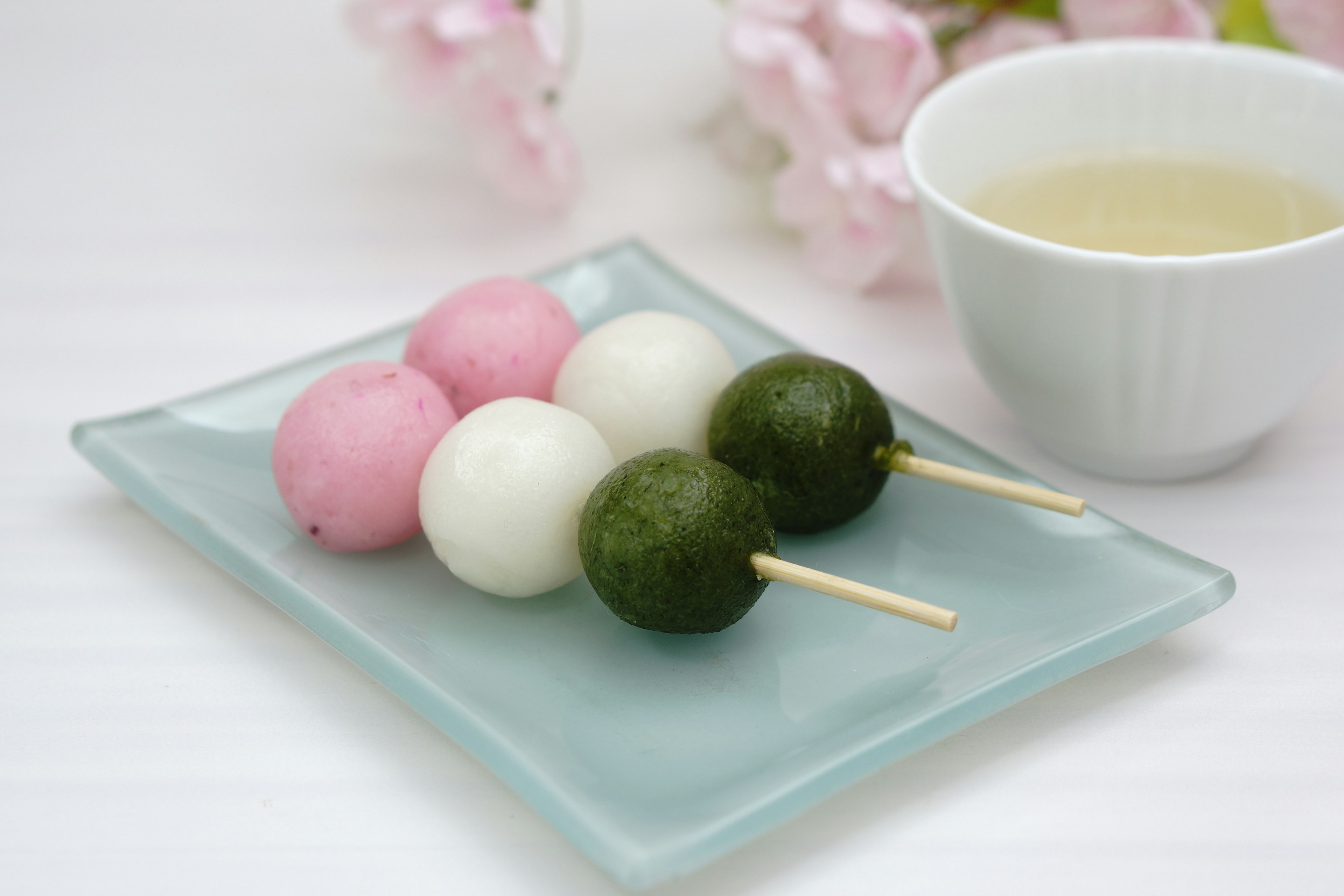 Dango berwarna disajikan dengan bunga sakura dan teh hijau