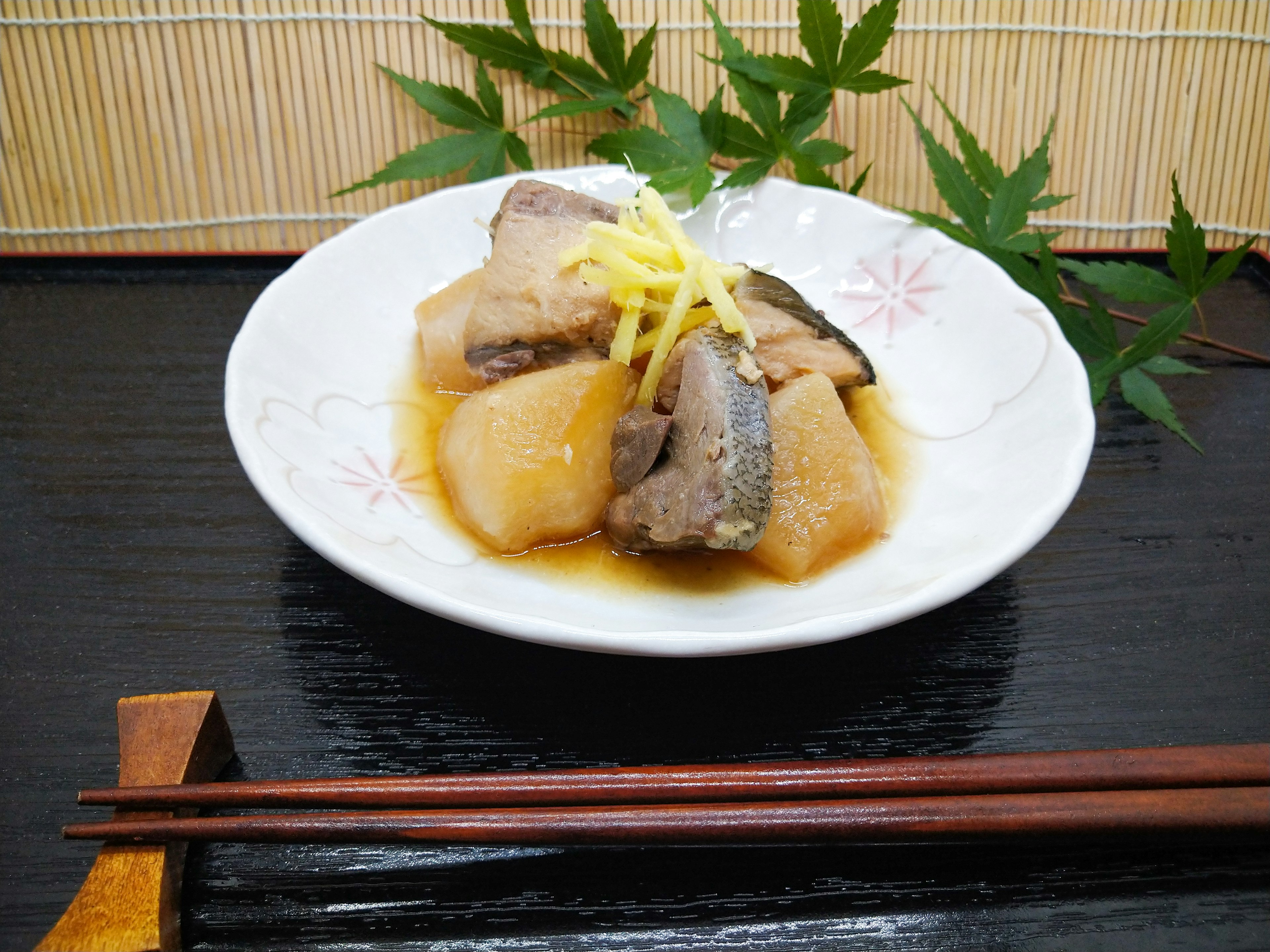 A dish of simmered fish and daikon garnished with sliced ginger on a white plate