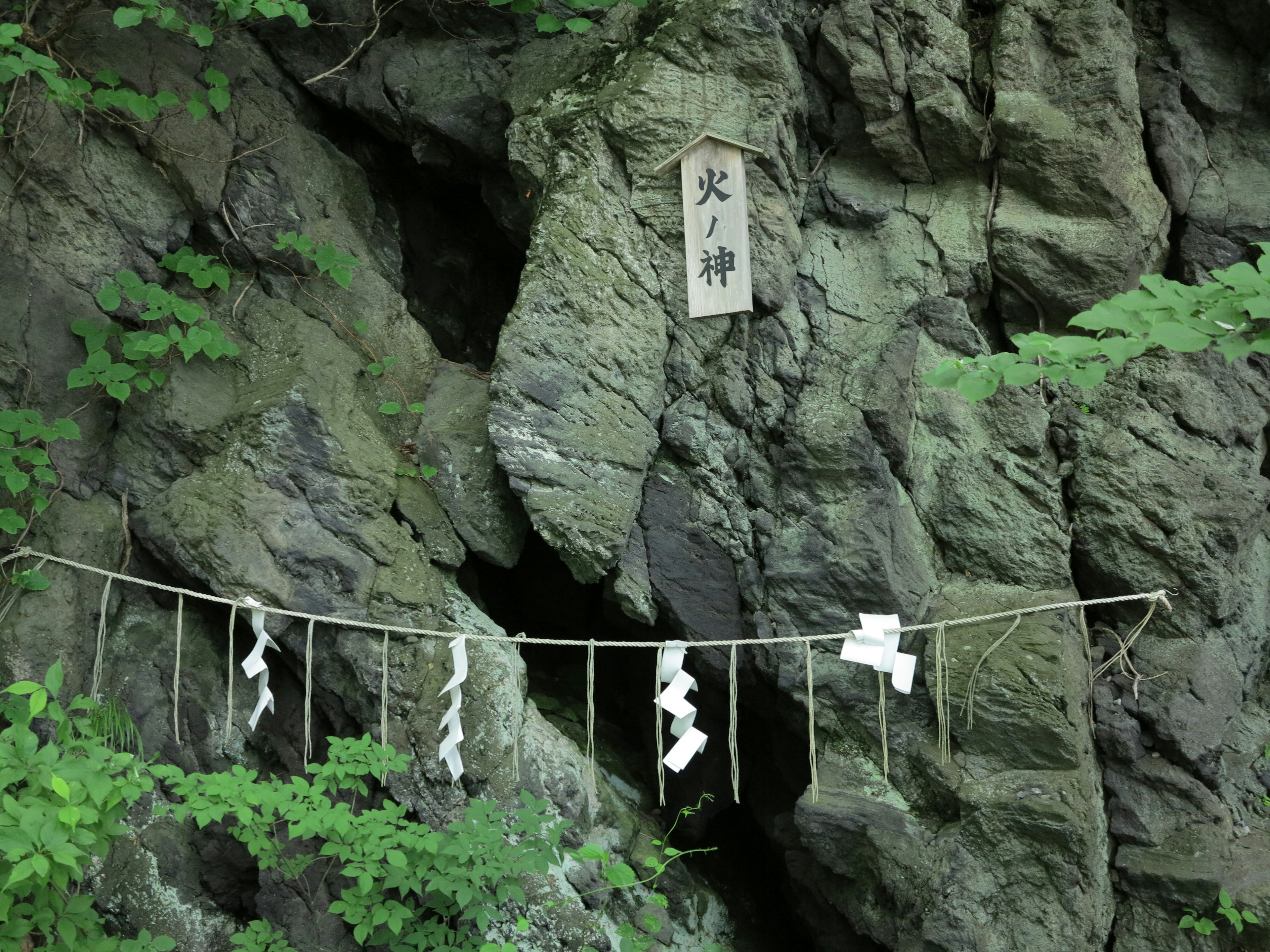 Natural landscape featuring a rock with white paper offerings and a sign