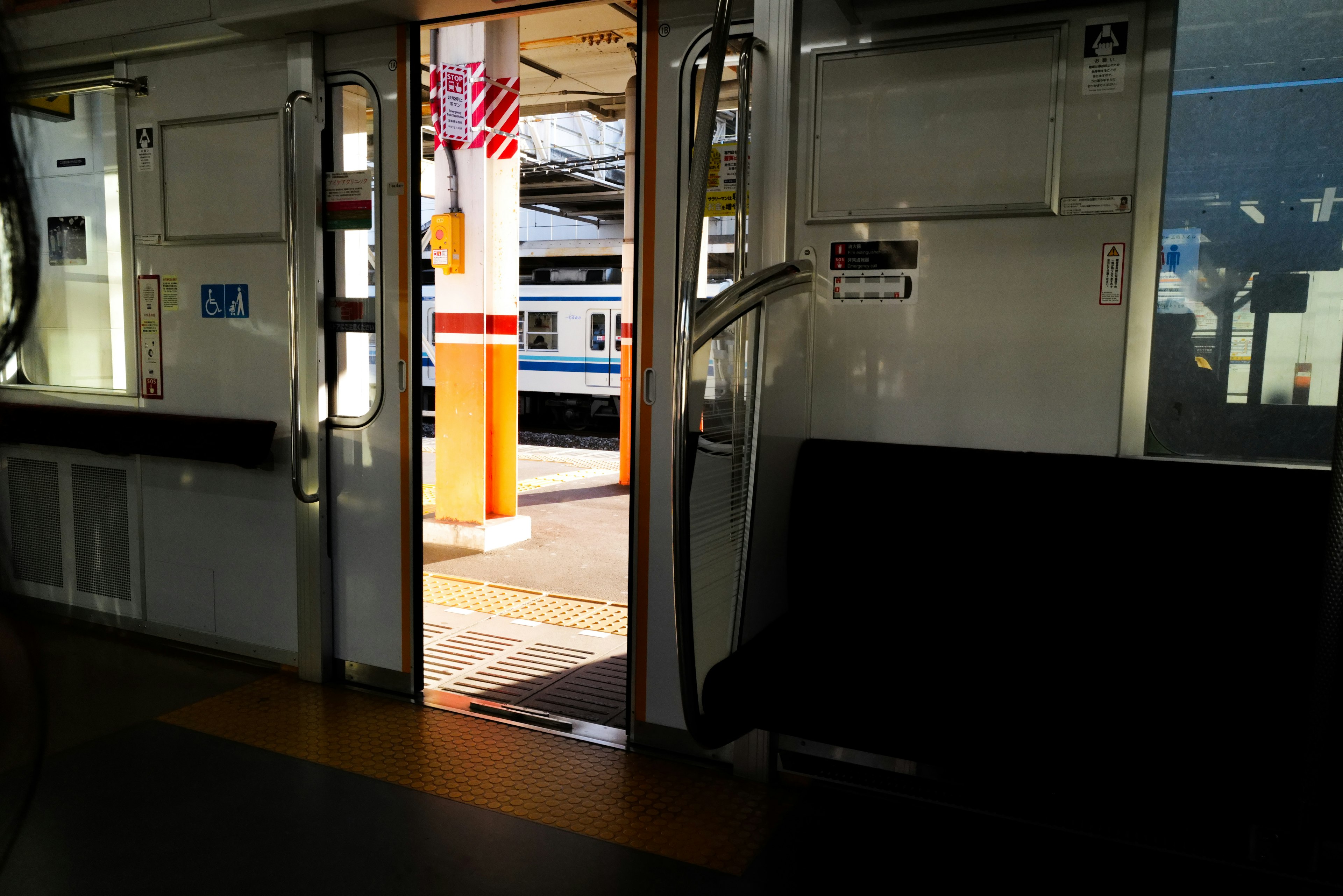 Vista desde dentro de un tren con una puerta abierta que muestra otro tren y la estructura de la estación afuera