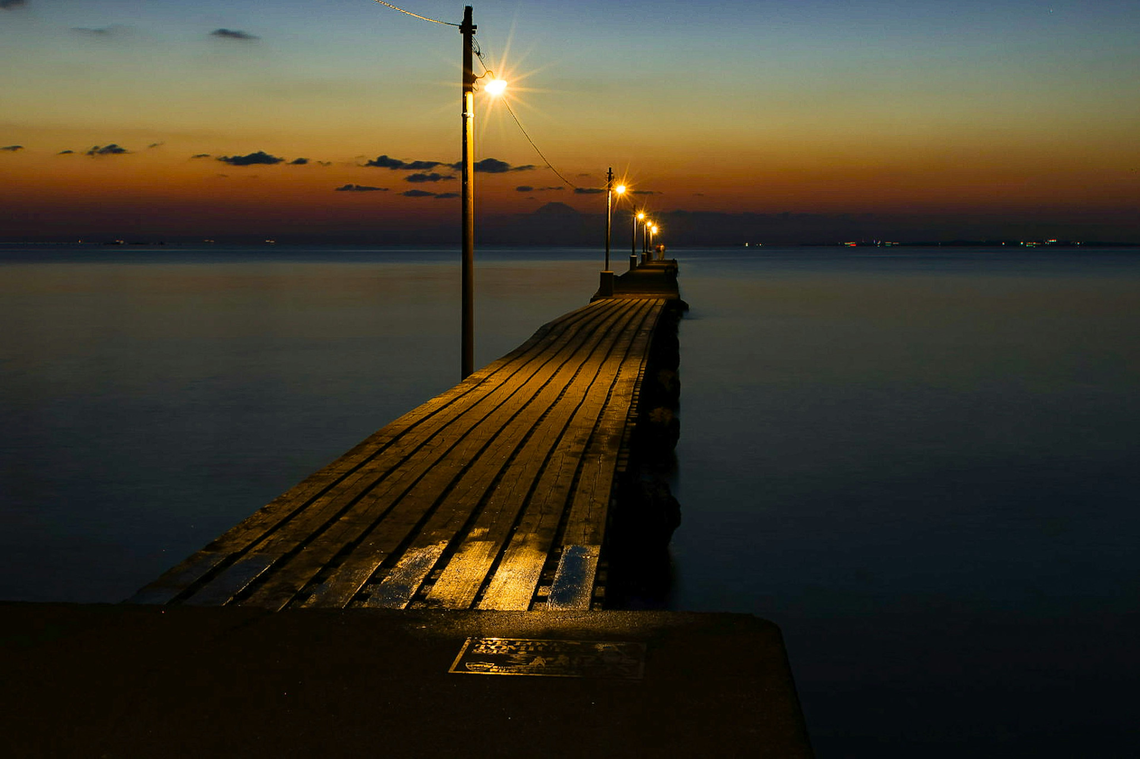 Dermaga yang membentang ke laut senja dengan lampu yang bersinar