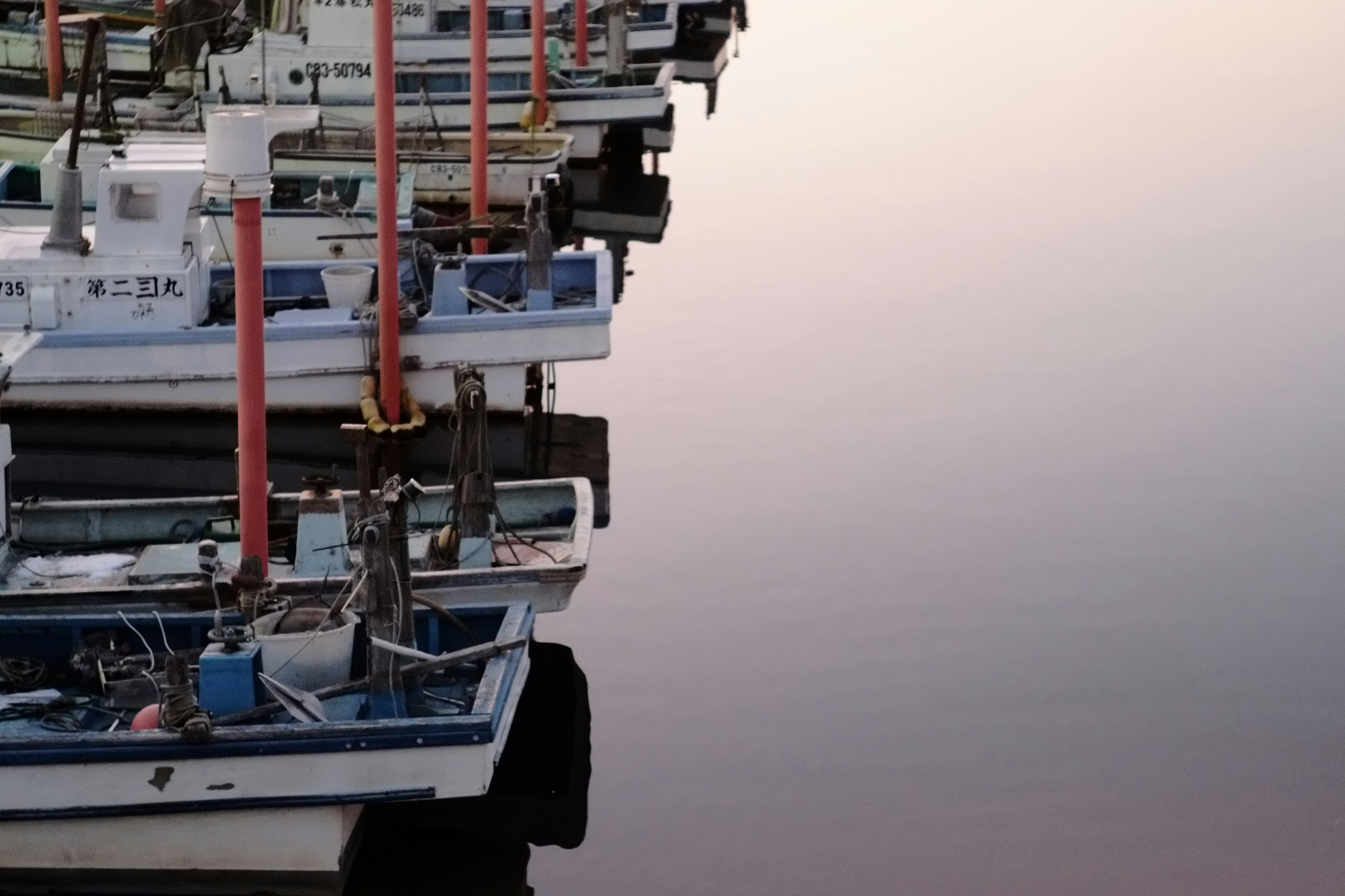 Fila de barcos de pesca con mástiles rojos reflejados en el agua tranquila