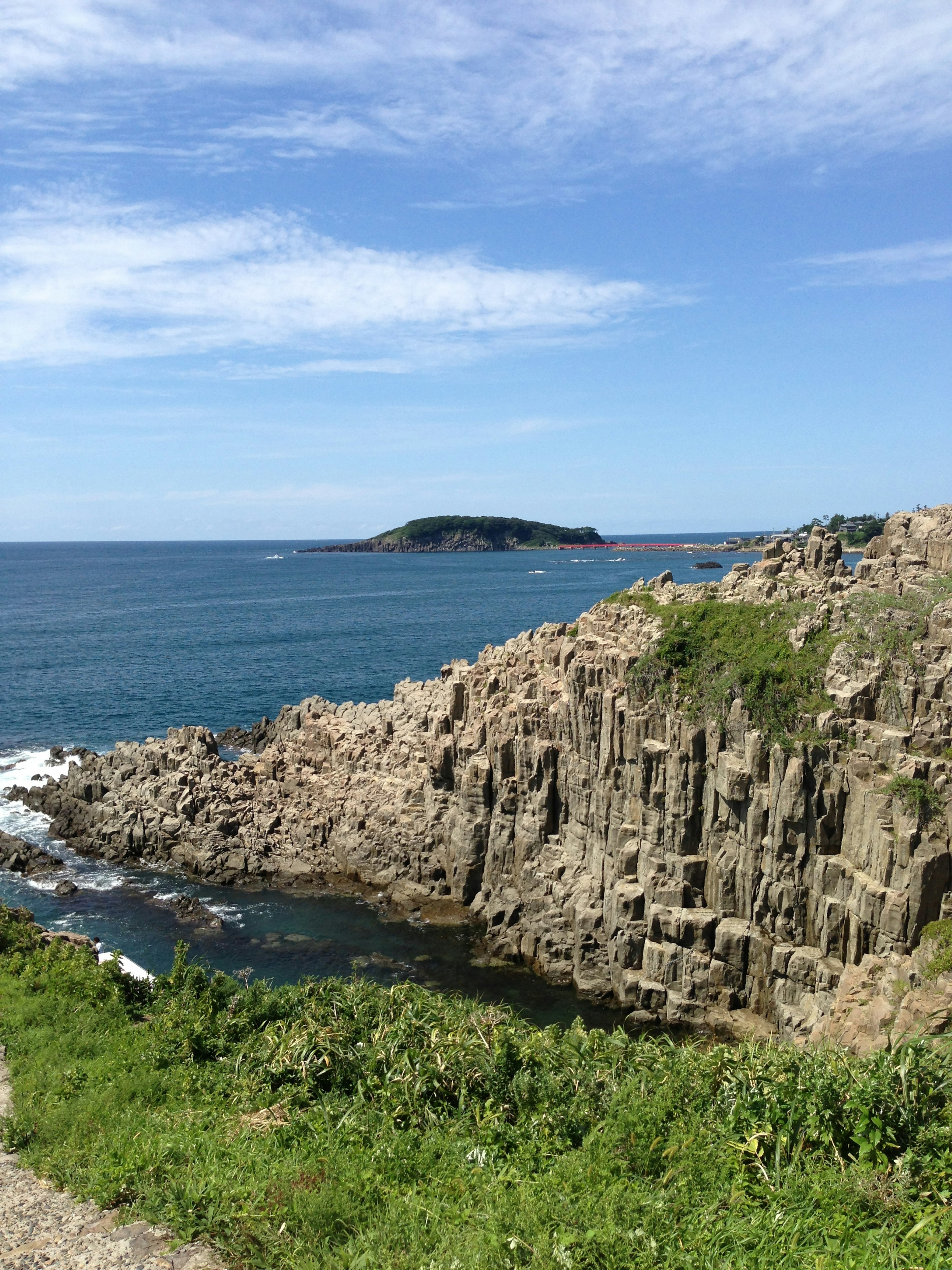 Scenic view of blue sea and rocky cliffs with a small island in the distance