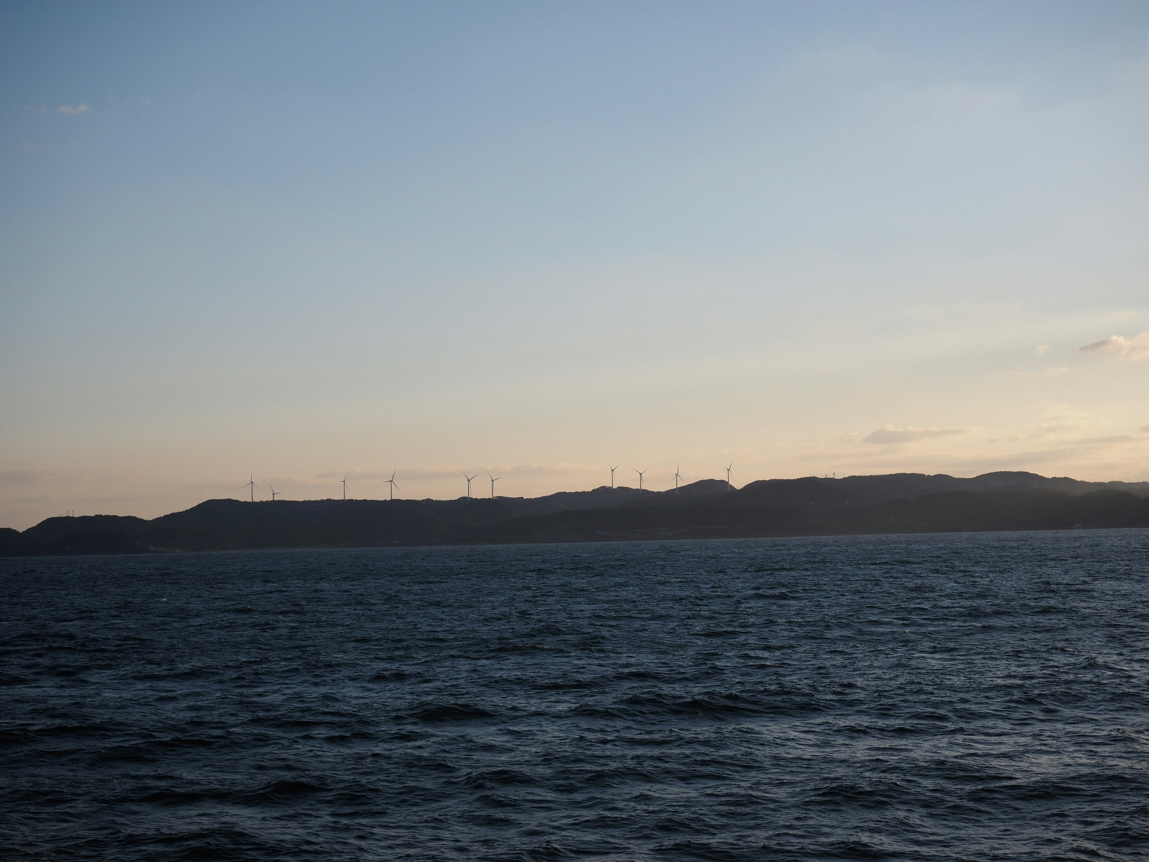 A sunset view with wind turbines along the horizon over the sea