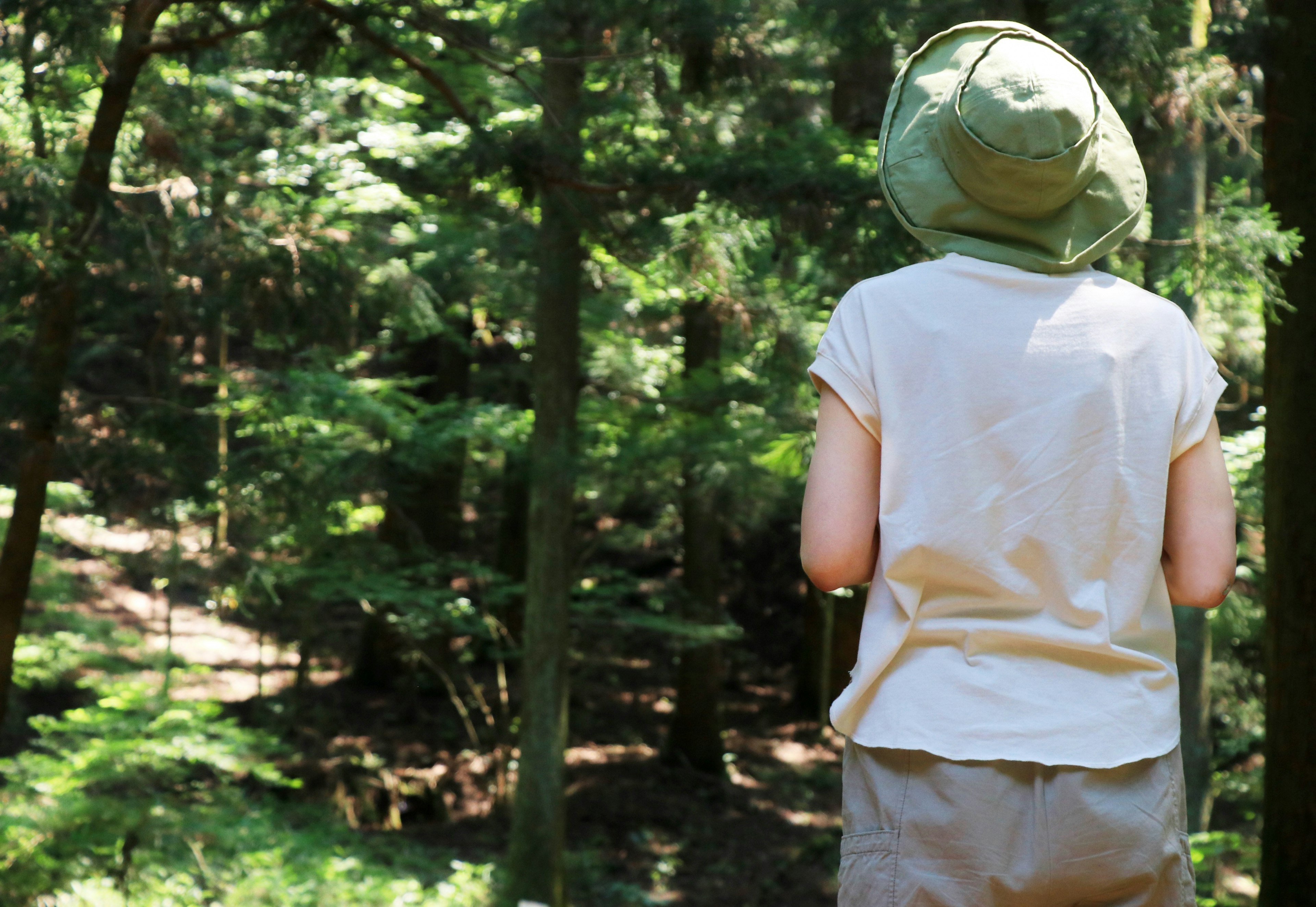 Person mit grünem Hut steht in einem Wald und schaut mit leichter Kleidung weg