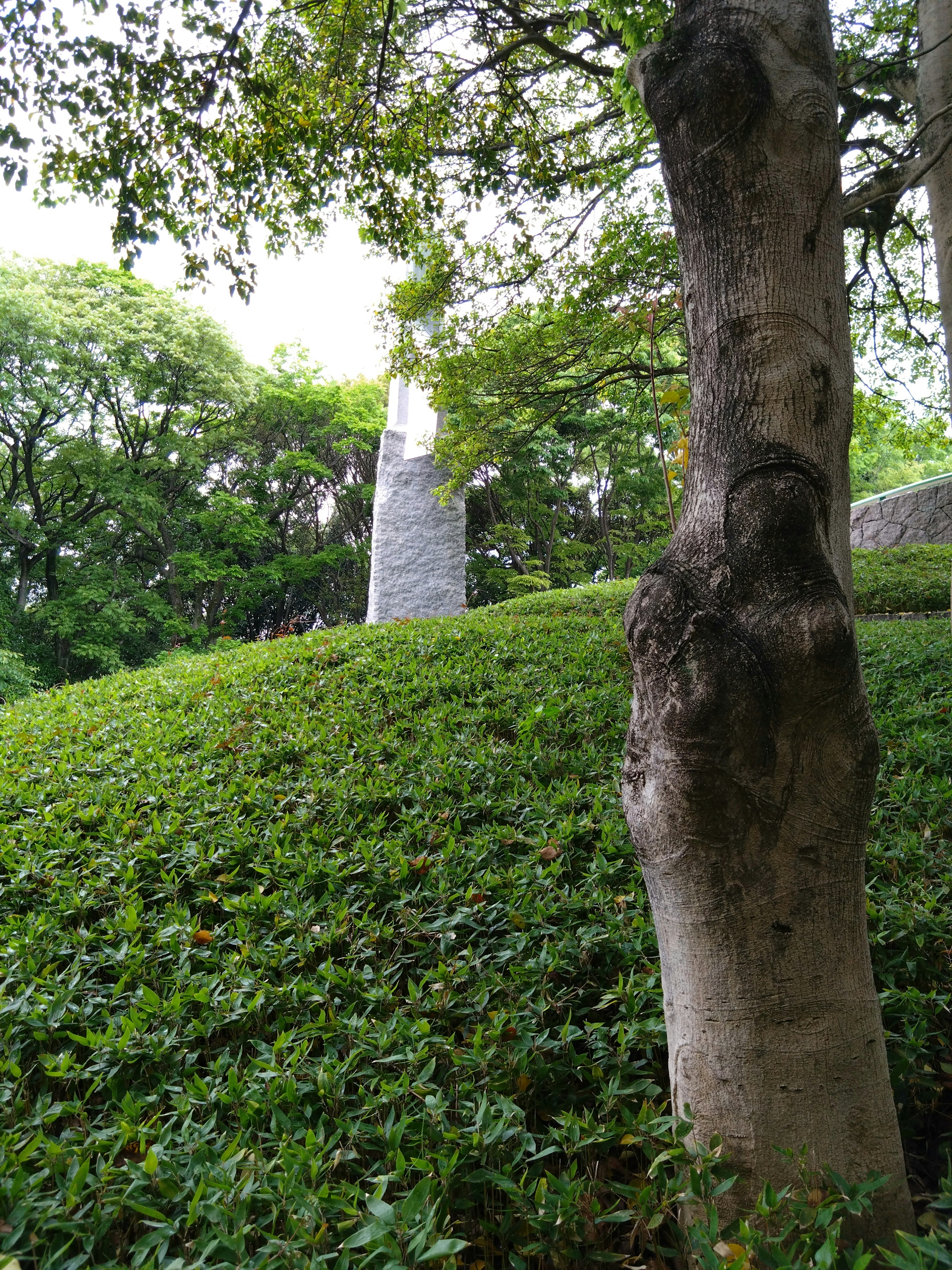 Stone sculpture near a green hill and tree