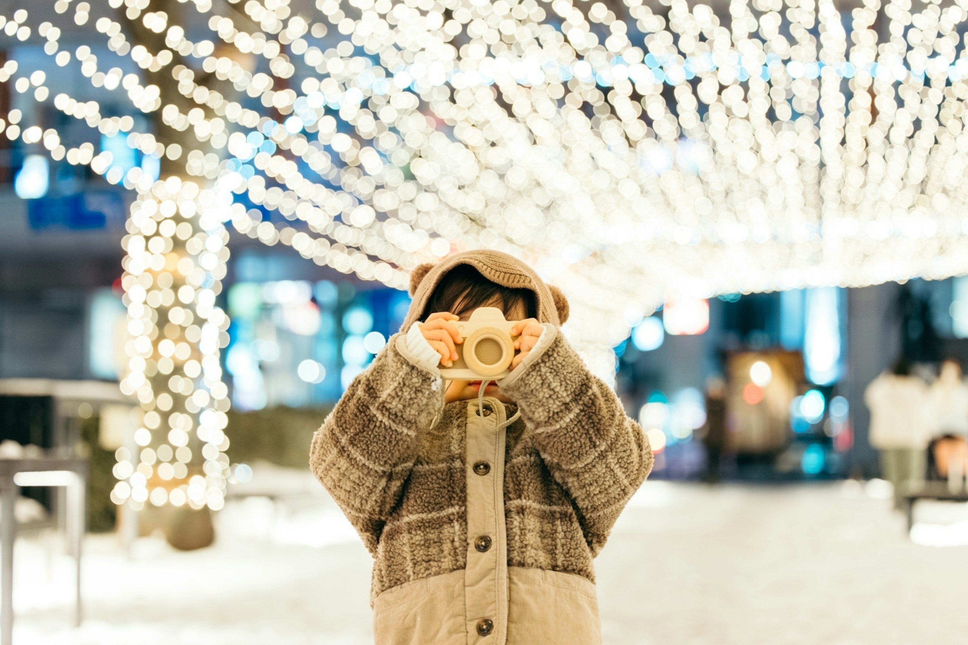 Child holding a camera under winter lights