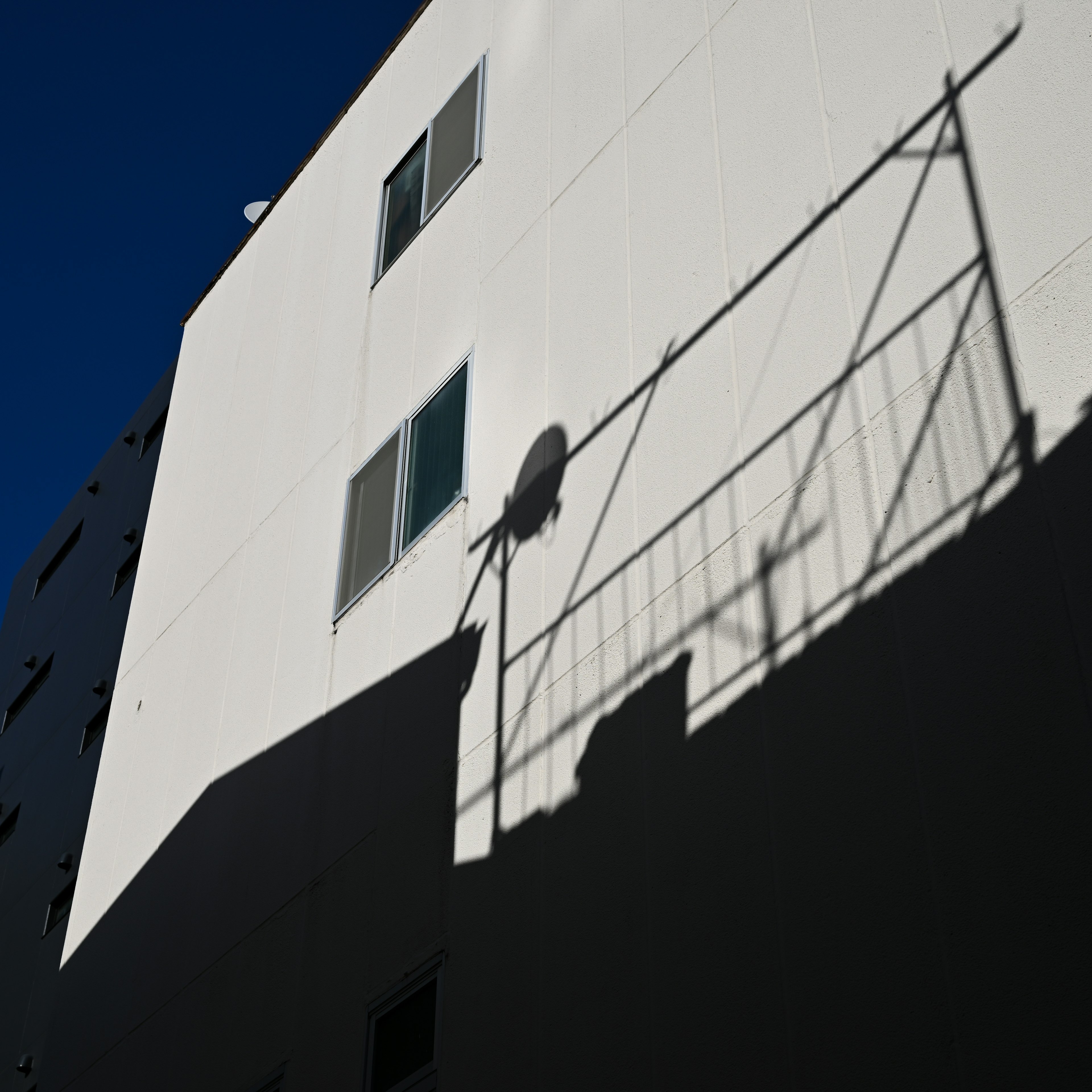 Schatten eines Geländers und einer Satellitenantenne an einer weißen Wand