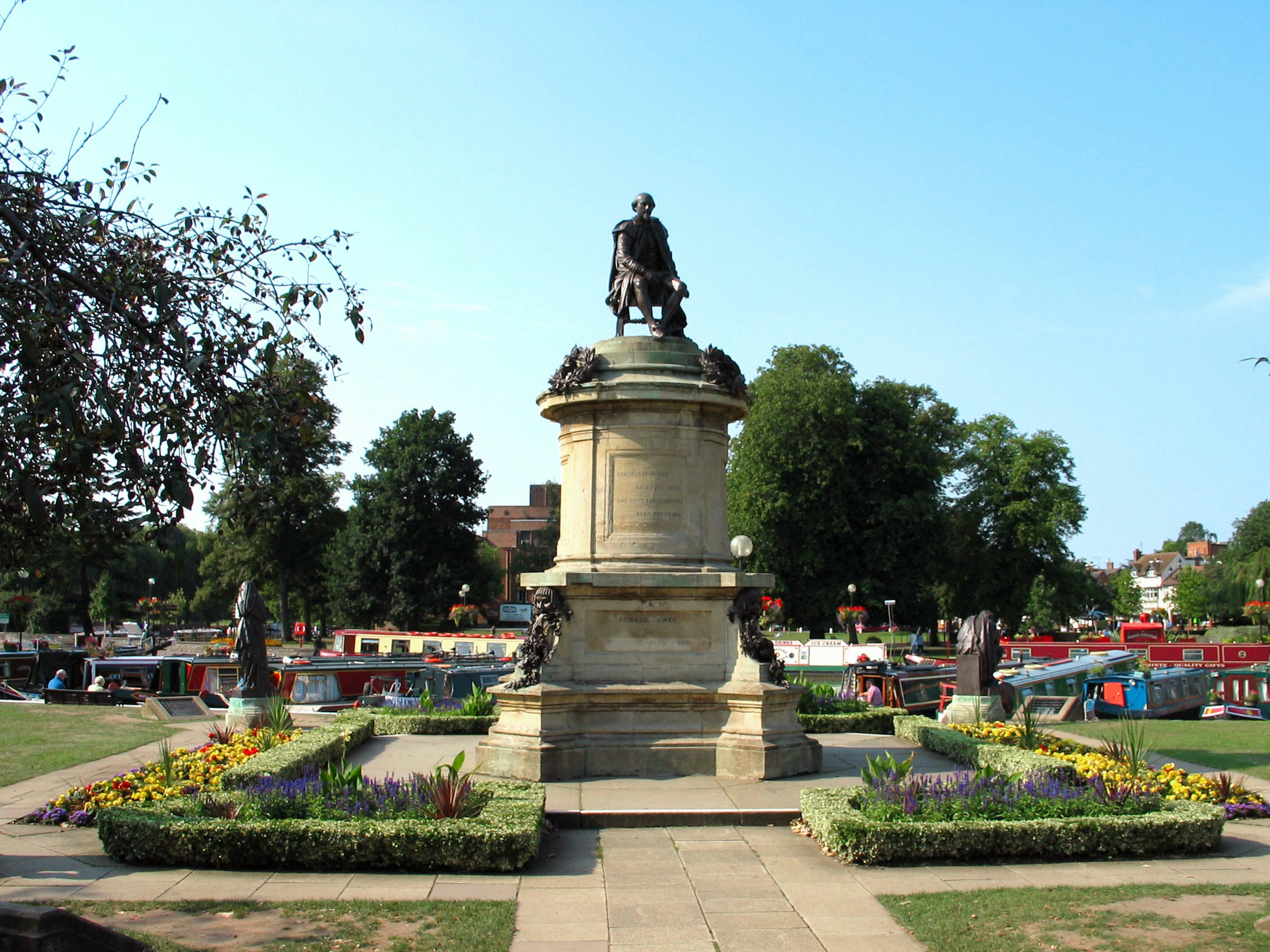 Statue in einem Park mit umliegenden Blumenbeeten und Booten