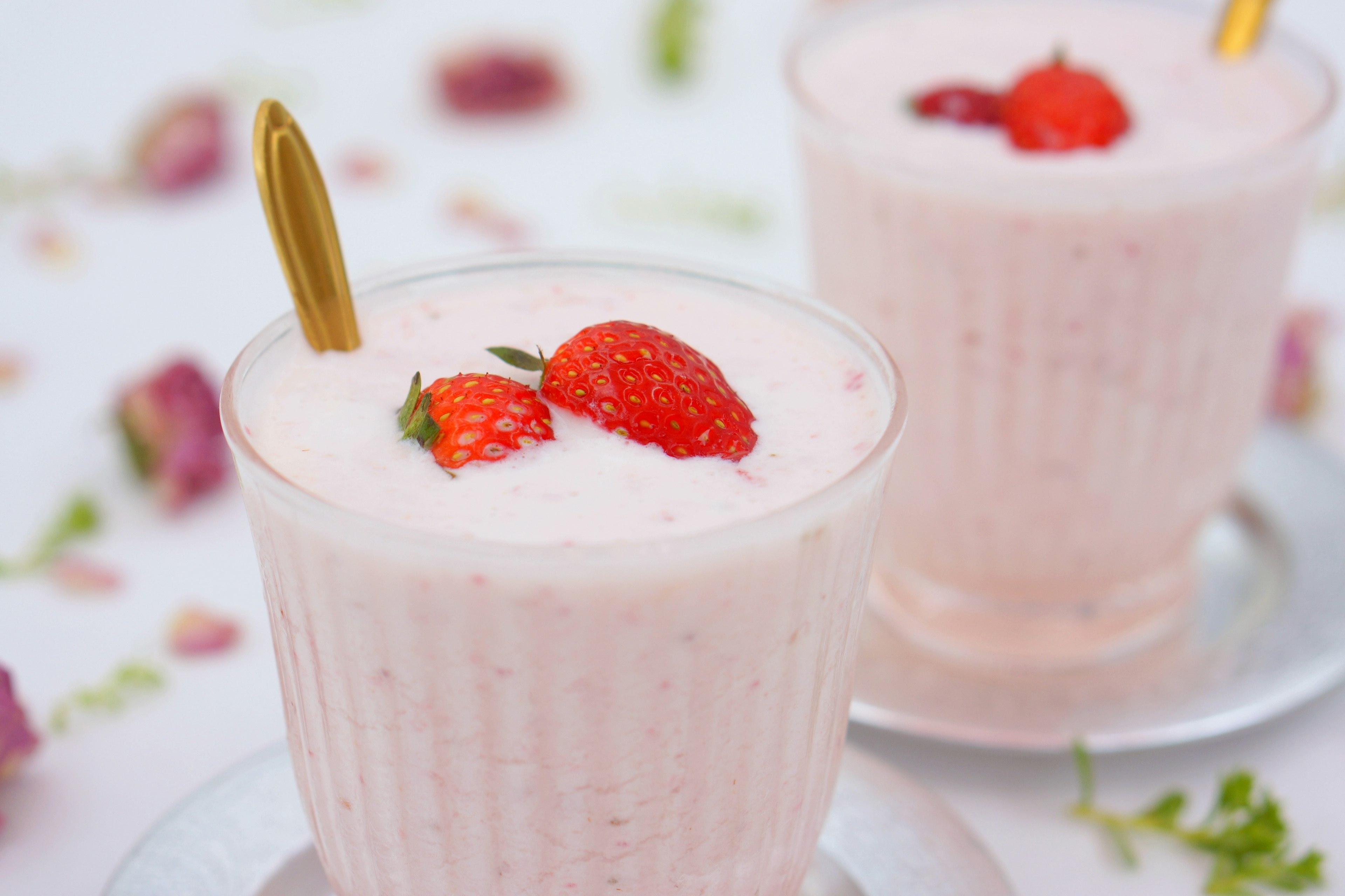 Cremiger Erdbeersmoothie in einem klaren Becher mit roten Erdbeeren garniert