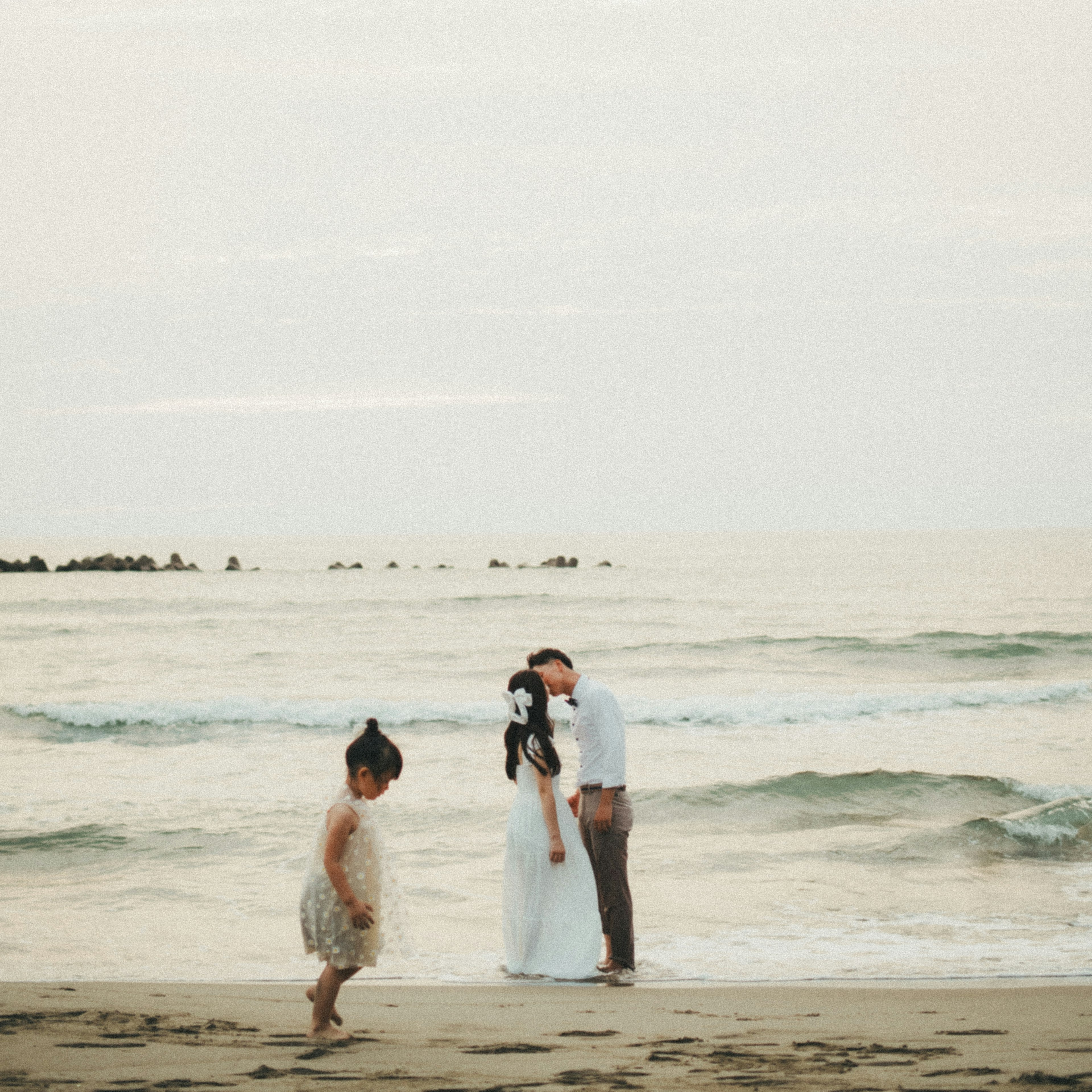 Pengantin berciuman di pantai dengan anak bermain di dekatnya