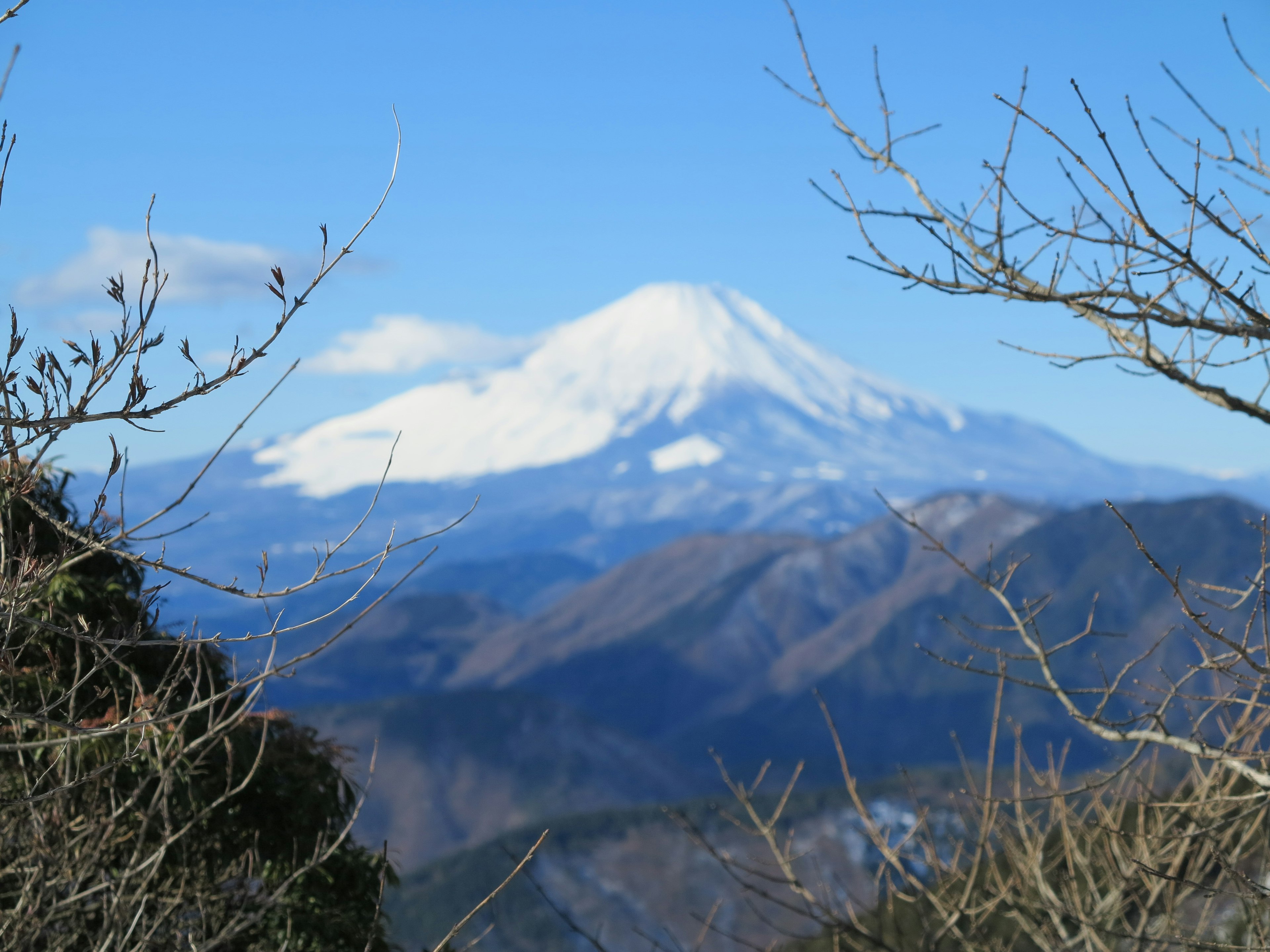 Monte Fuji coperto di neve sotto un cielo blu con montagne circostanti