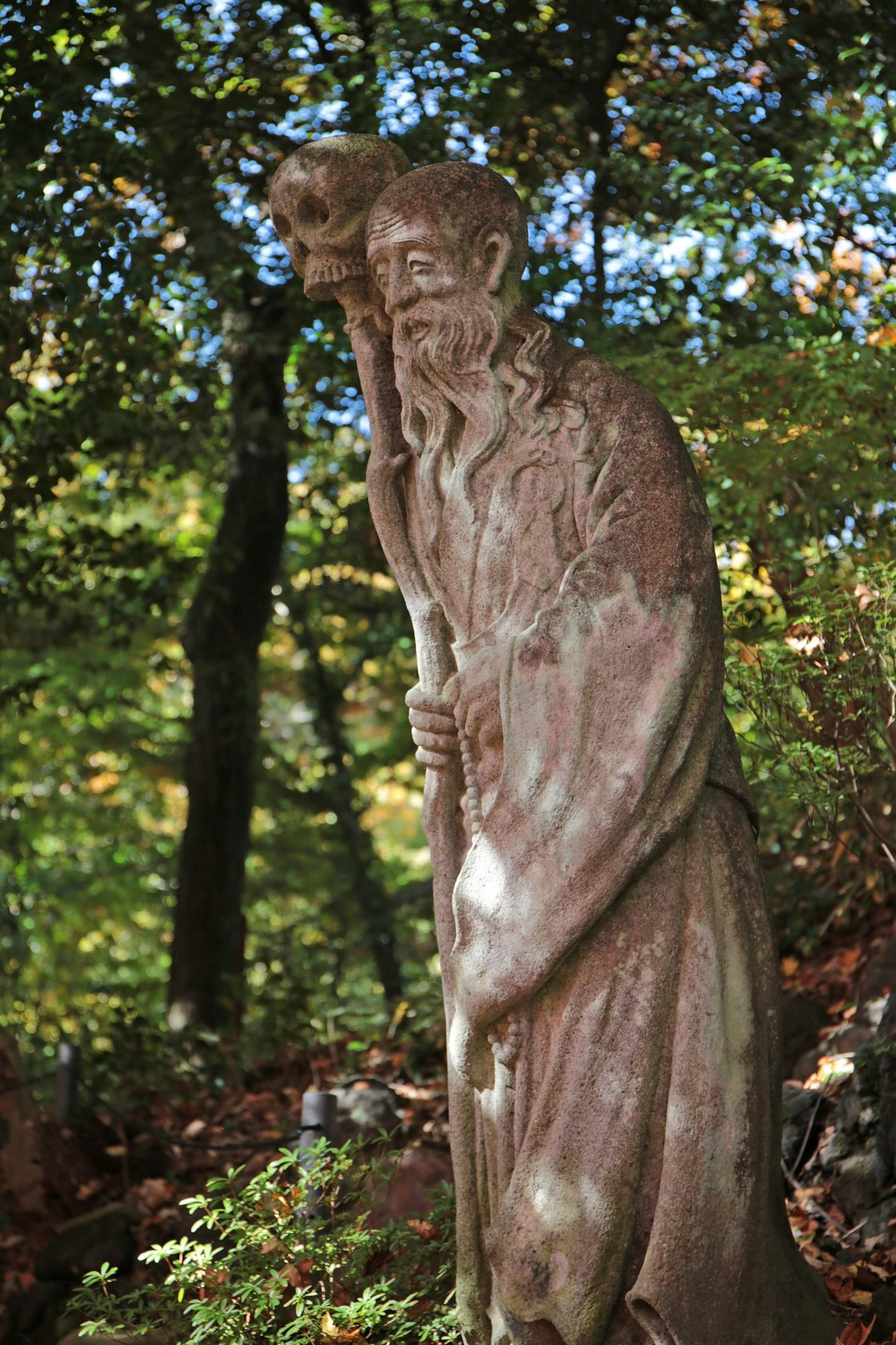 Une vieille statue d'un homme tenant un bâton se tenant dans une zone boisée