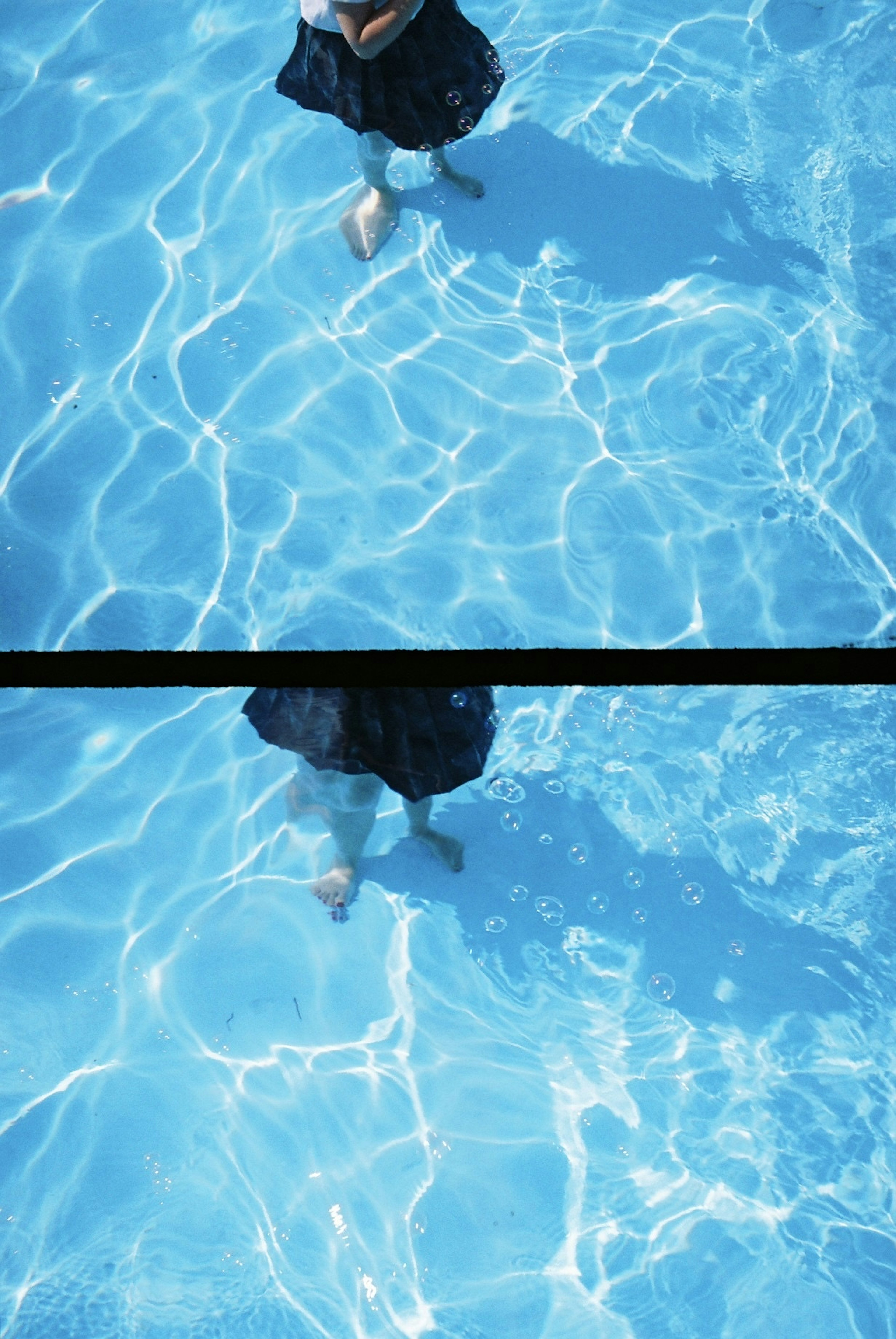 Person's feet standing in a blue swimming pool water