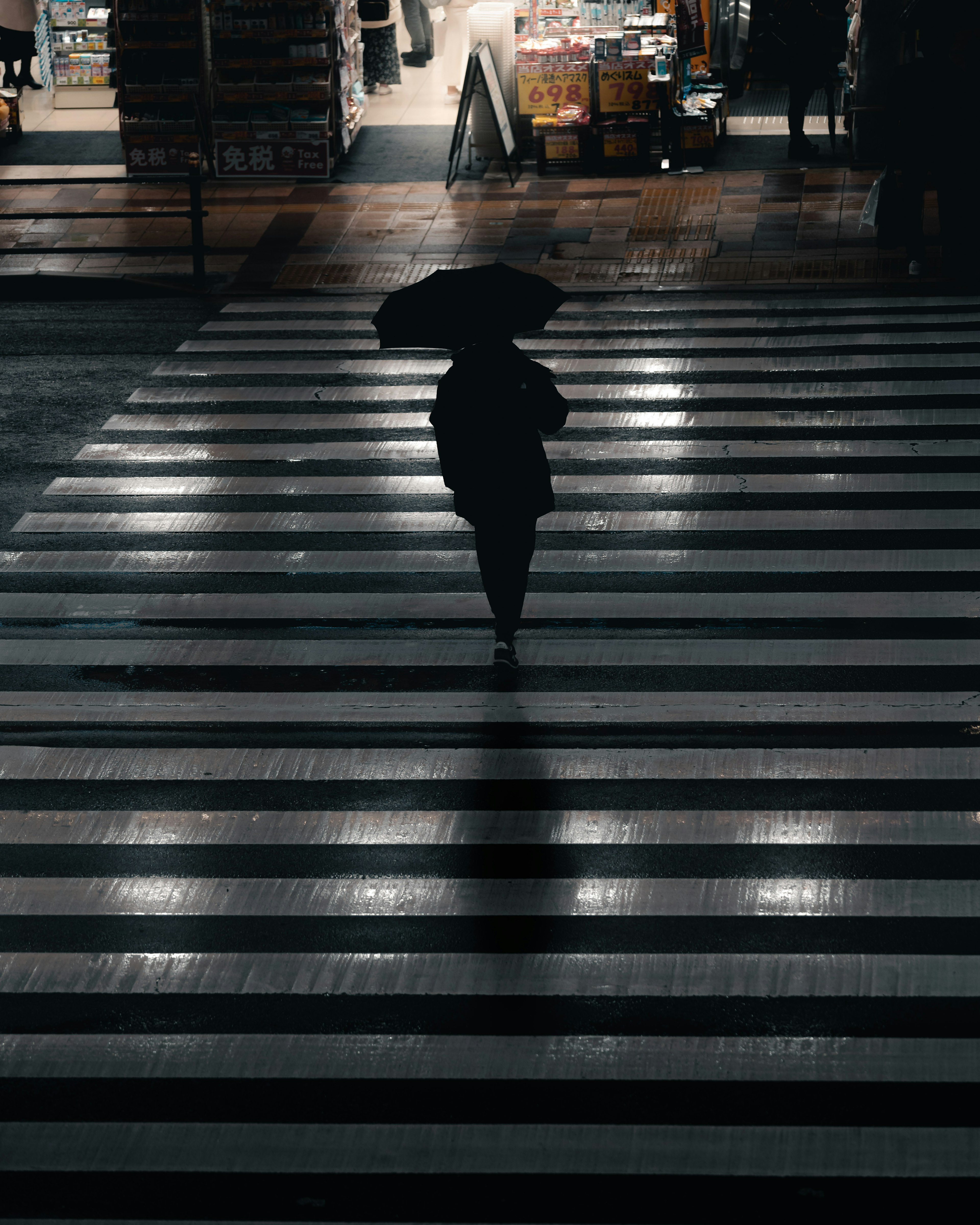 Eine Person mit einem Regenschirm, die nachts über einen Zebrastreifen geht