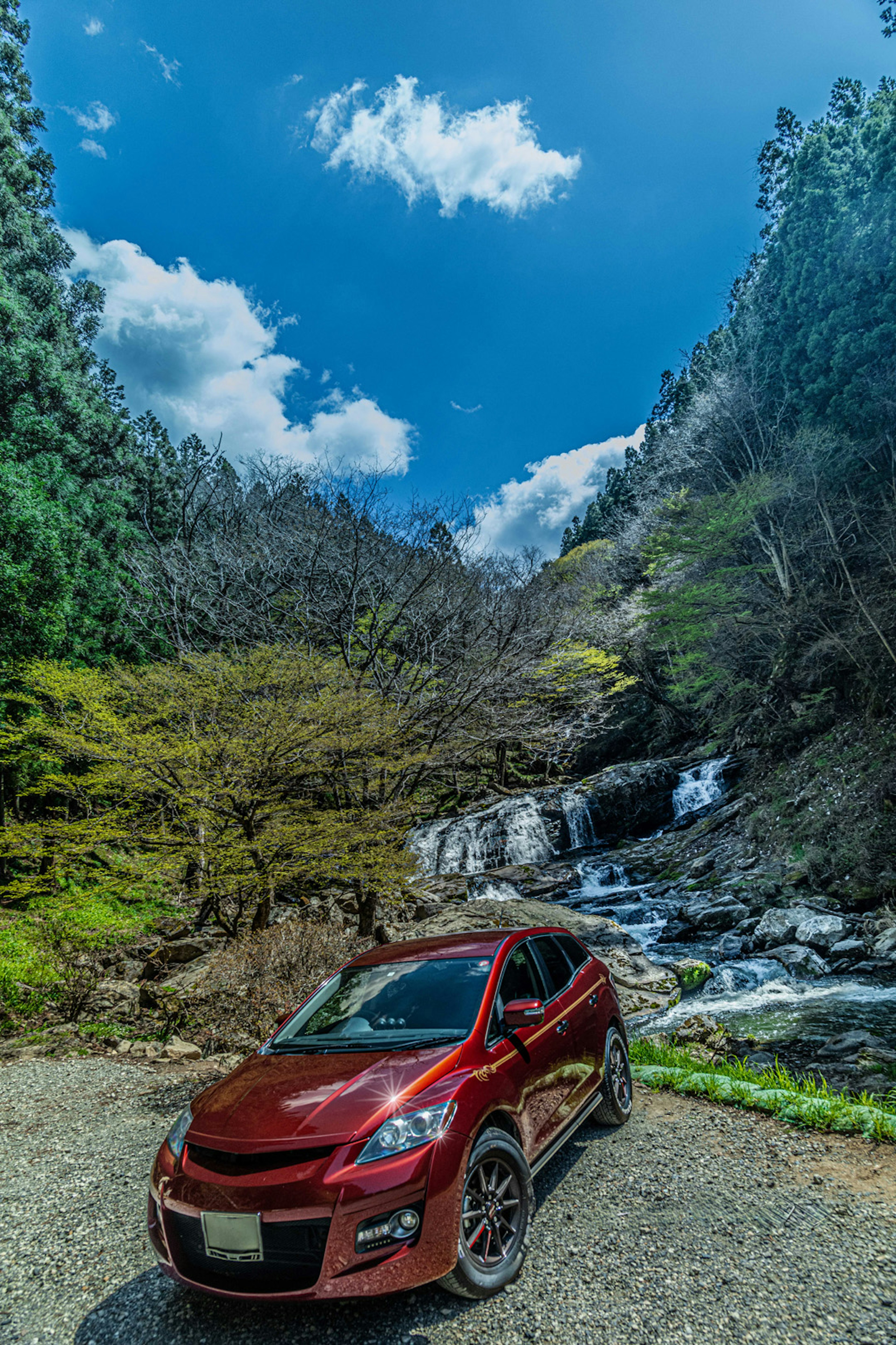 Rotes Auto, das in einer natürlichen Umgebung neben einem Wasserfall parkt