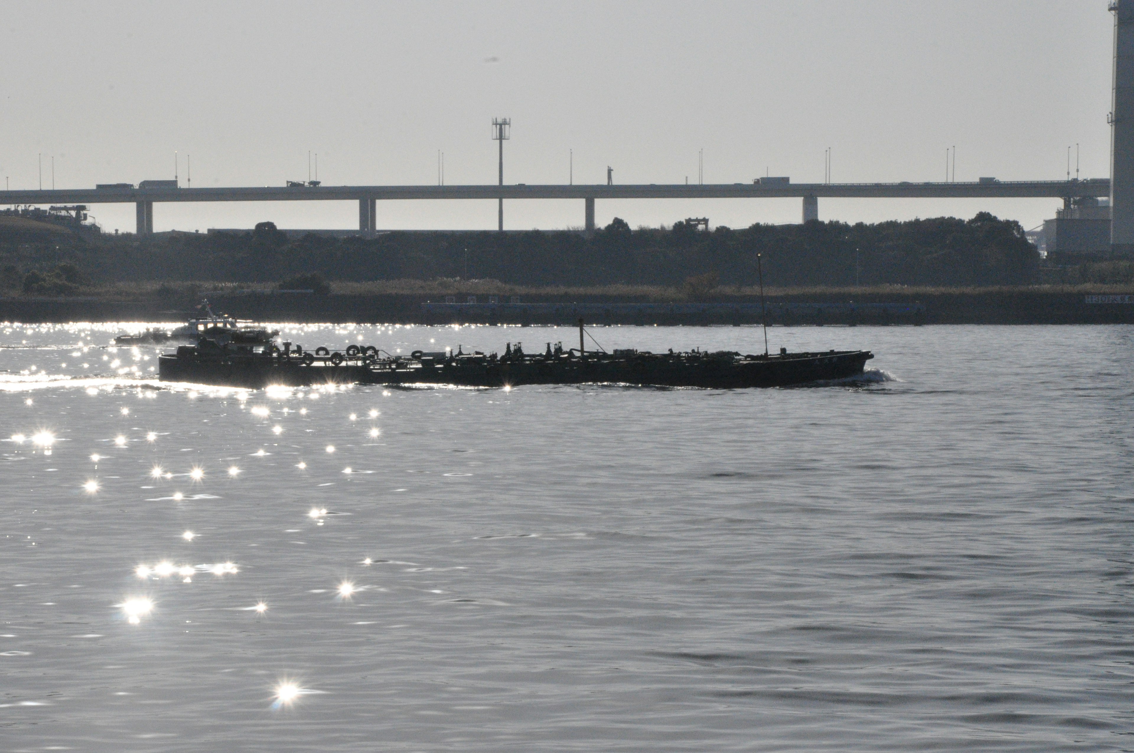 Silhouette eines Bootes auf schimmerndem Wasser mit einer Brücke im Hintergrund