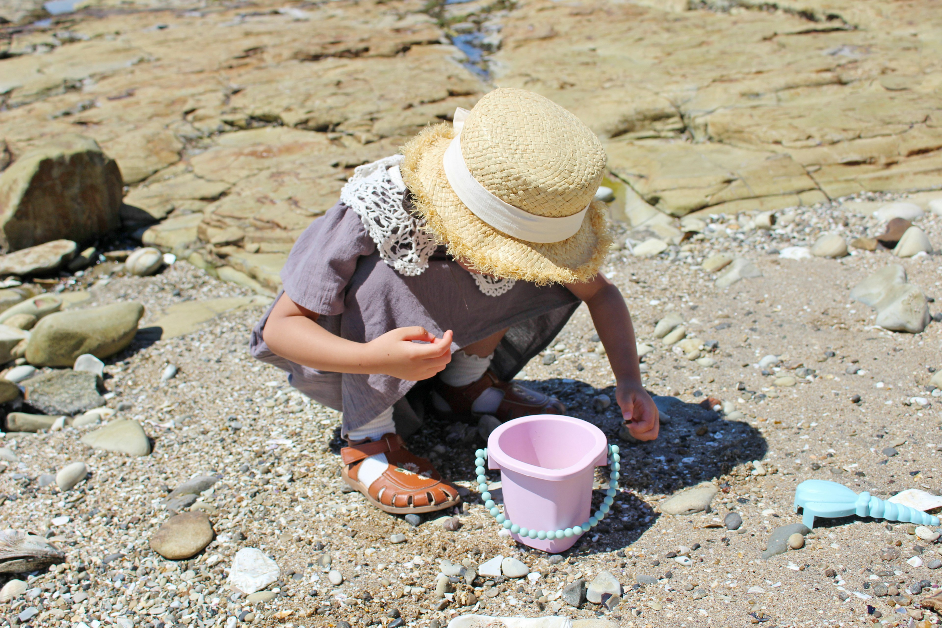 孩子在海滩上用粉色桶和周围的卵石挖沙子