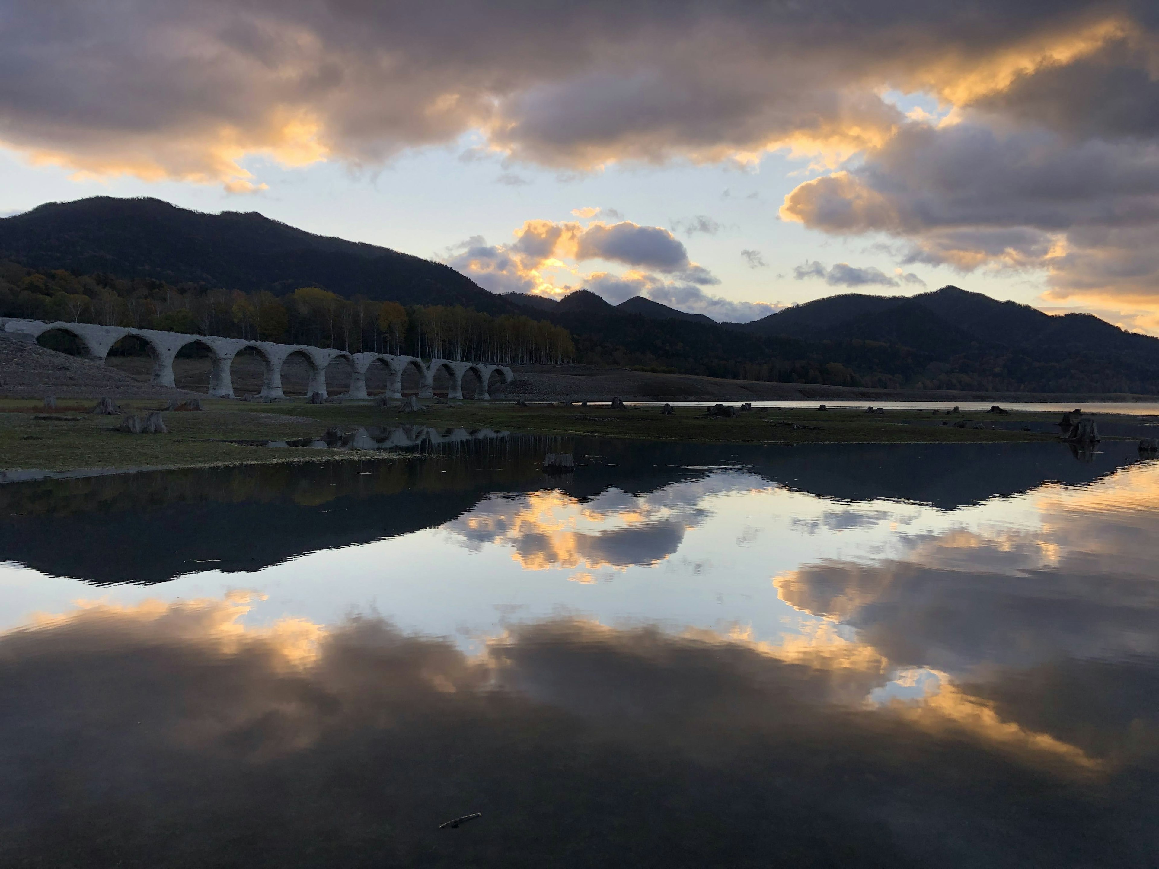 Scenic view of a lake reflecting a beautiful sunset and mountains with an arch bridge