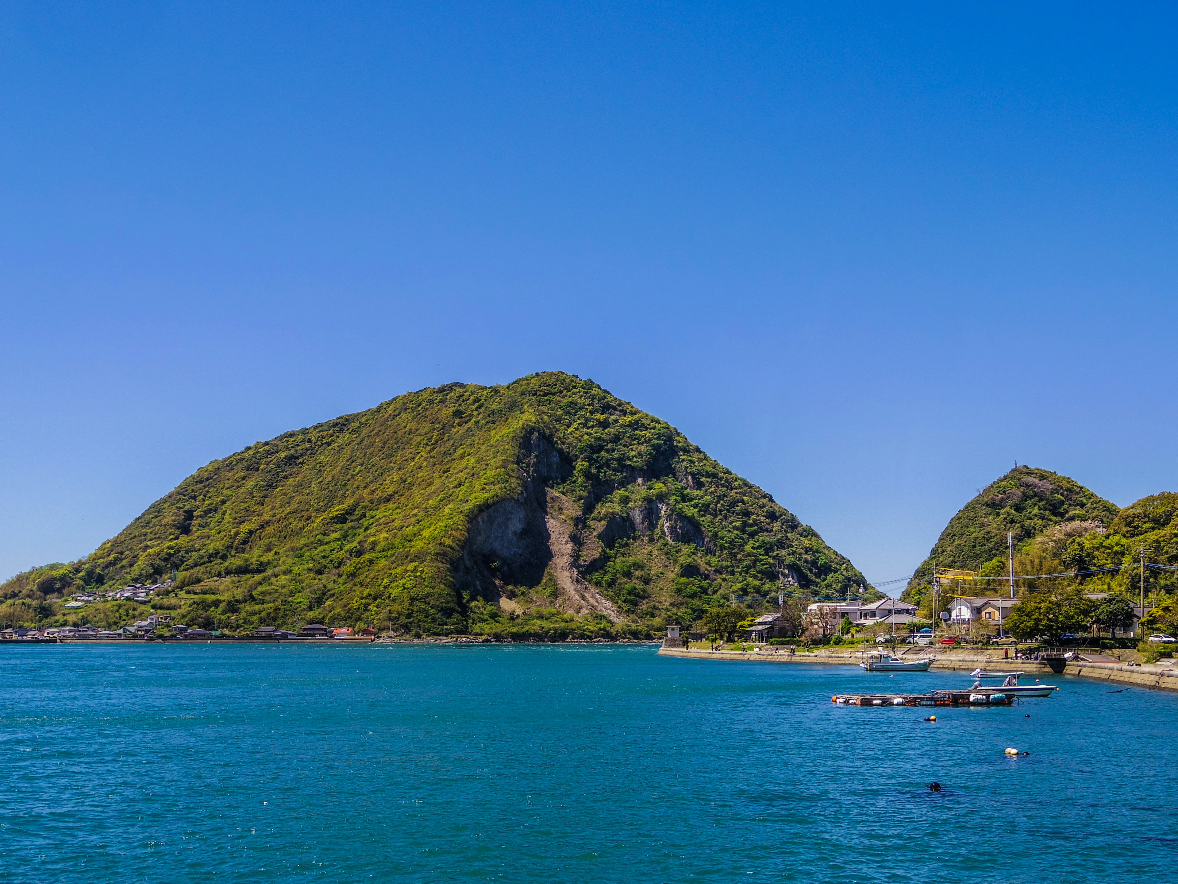 Vue pittoresque de collines vertes entourées par une mer bleue et un petit village de pêcheurs