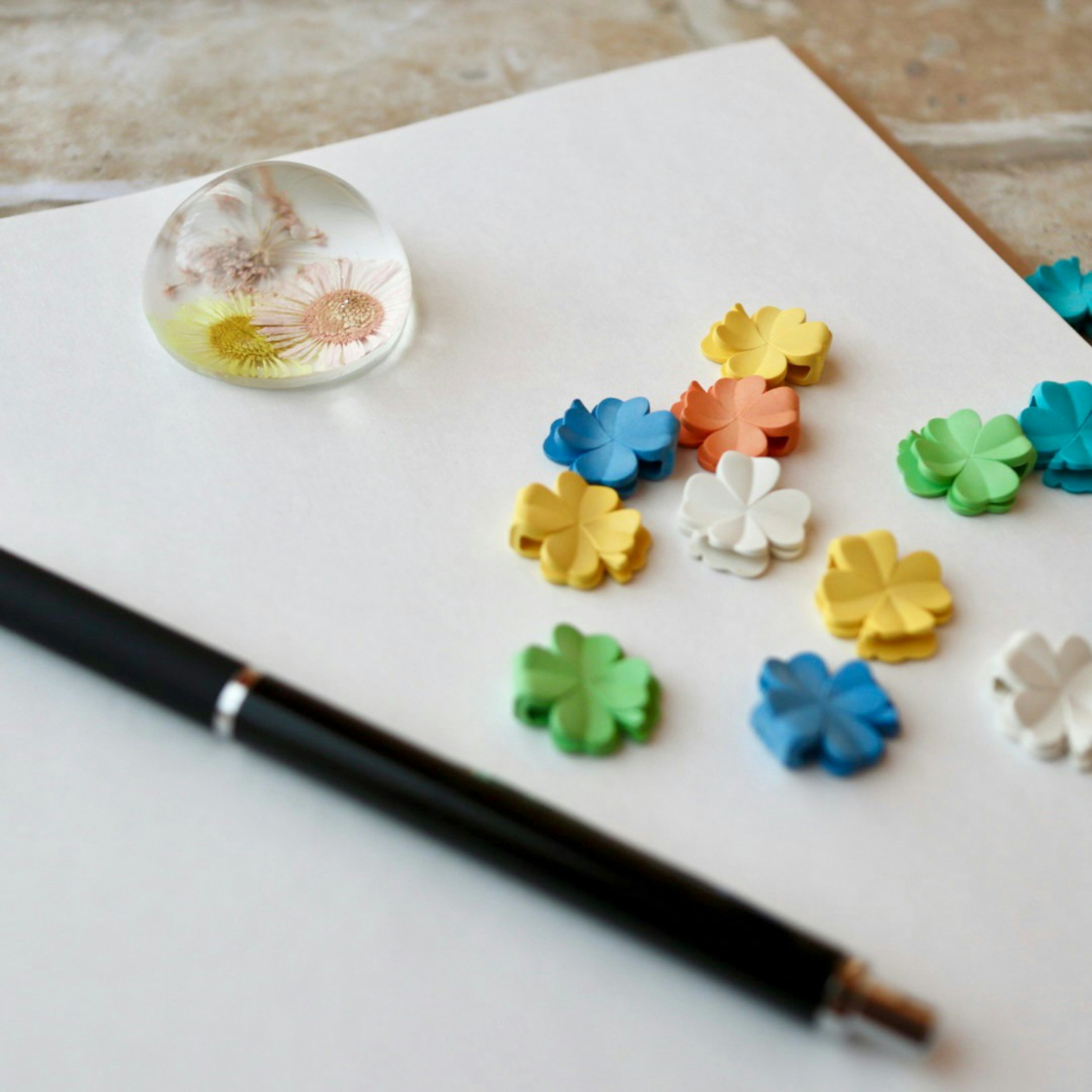 Colorful flower-shaped decorations and a pen on white paper