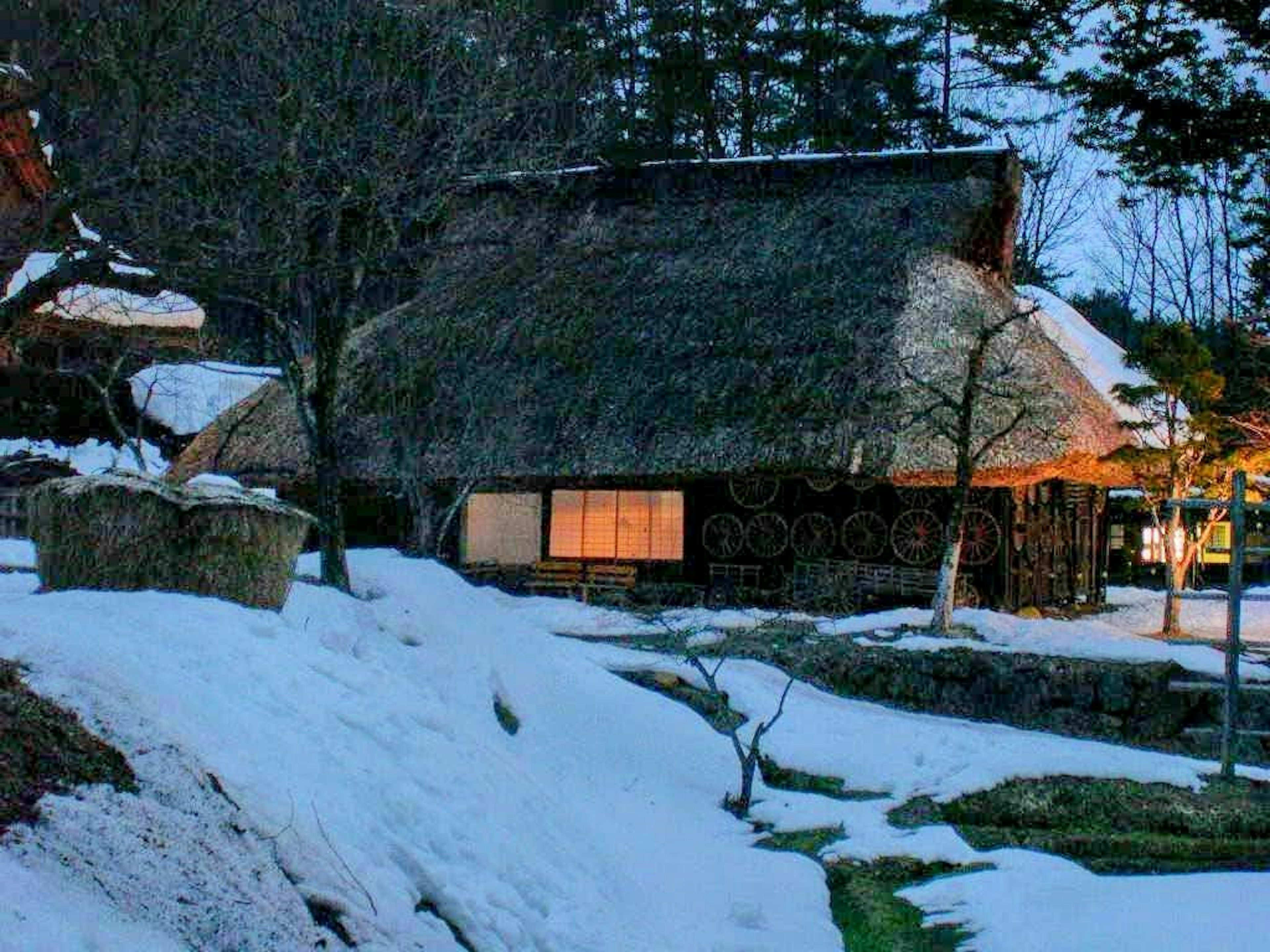 Casa tradicional japonesa con techo de paja rodeada de nieve y árboles