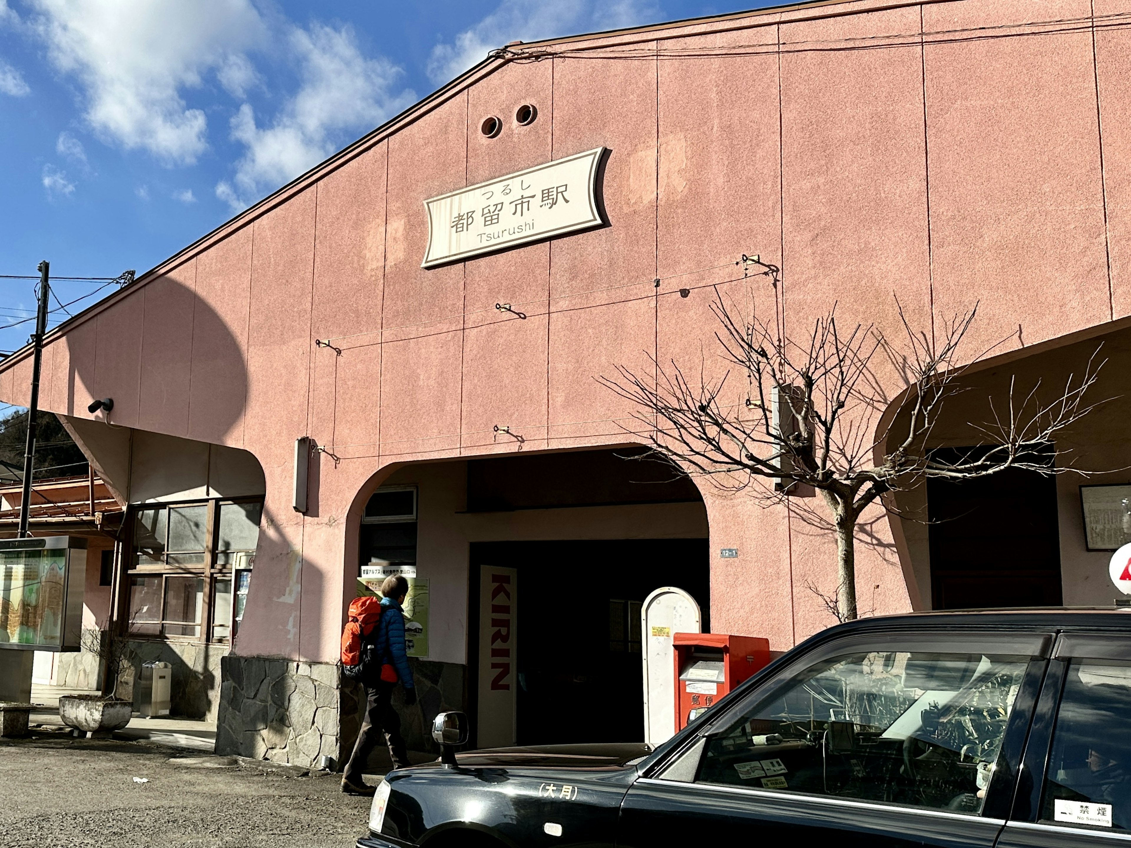 ピンクの外壁を持つ駅の建物と人が歩いている風景