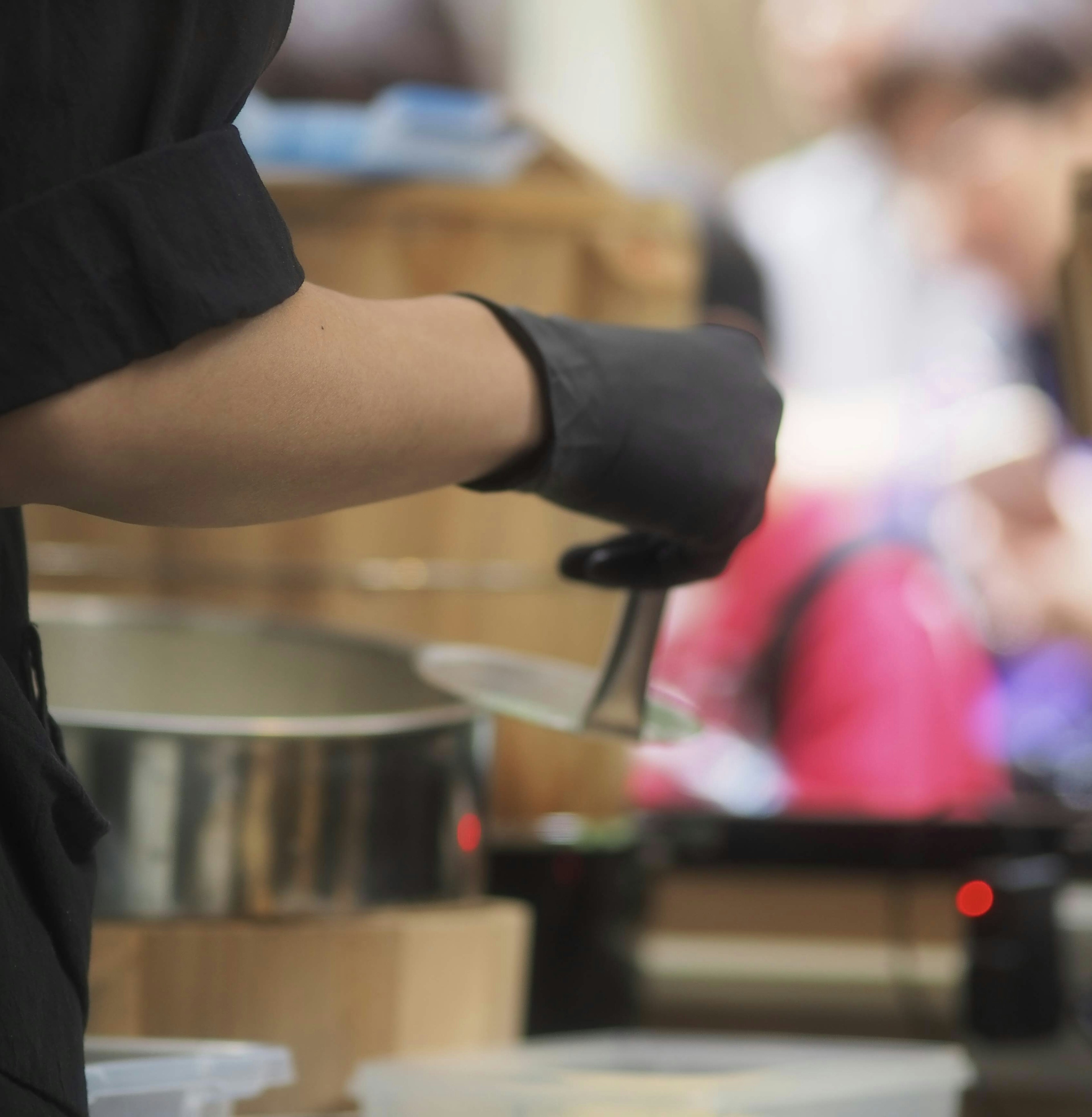 Sebuah tangan yang mengenakan sarung tangan hitam memegang alat masak dalam adegan persiapan makanan