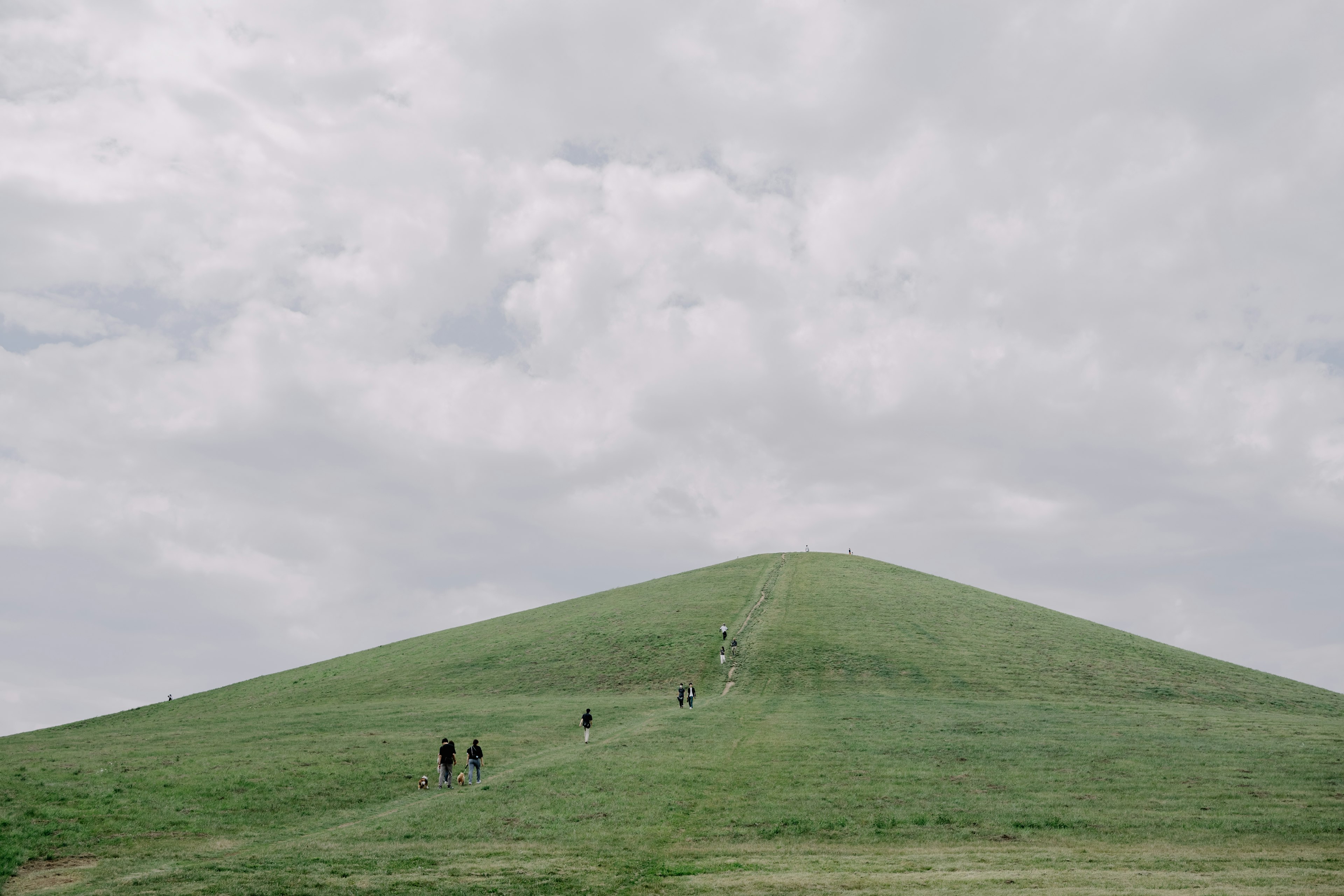 緑の丘を登る人々と曇り空の風景