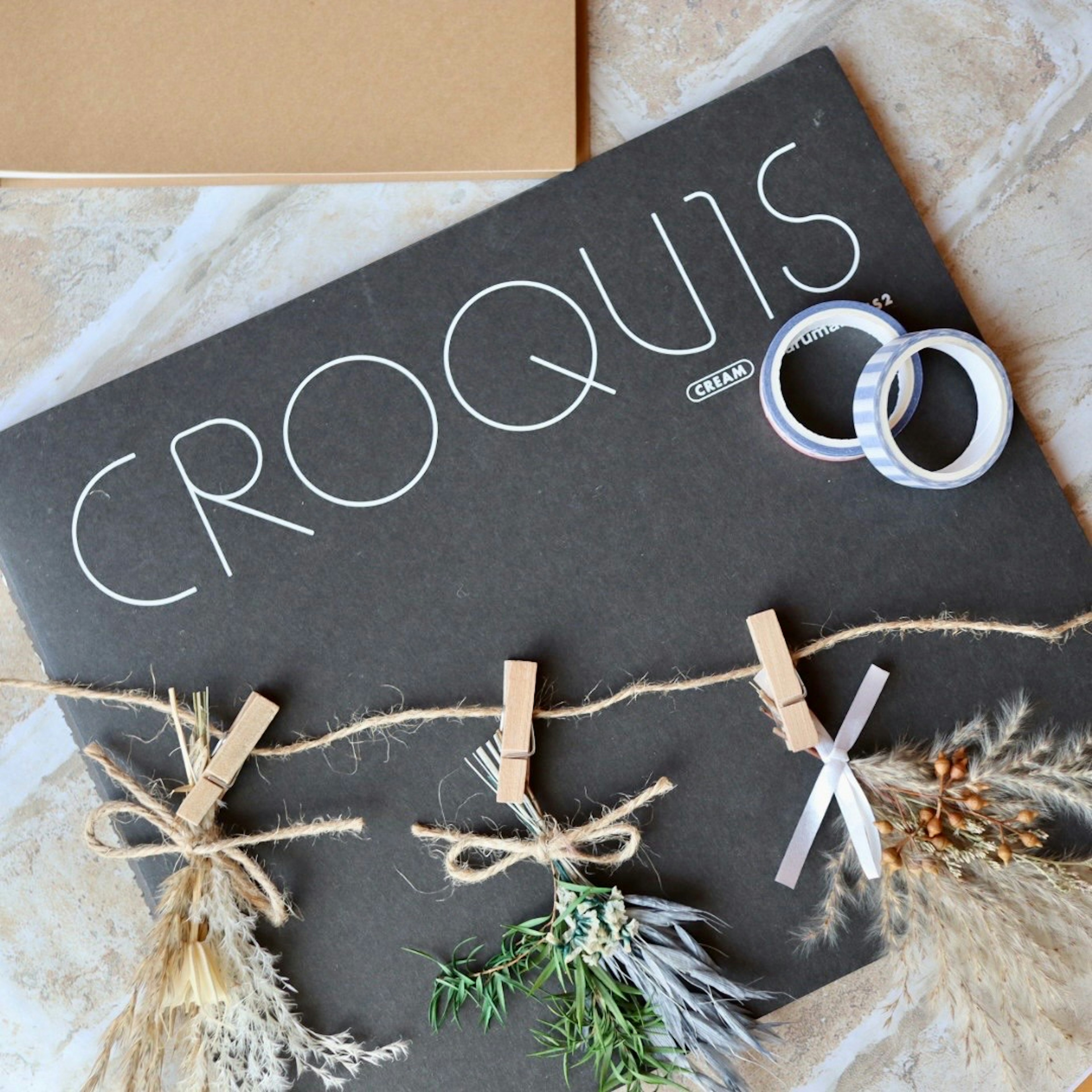 A sketchbook titled 'CROQUIS' on a black background with dried flowers clipped on a twine