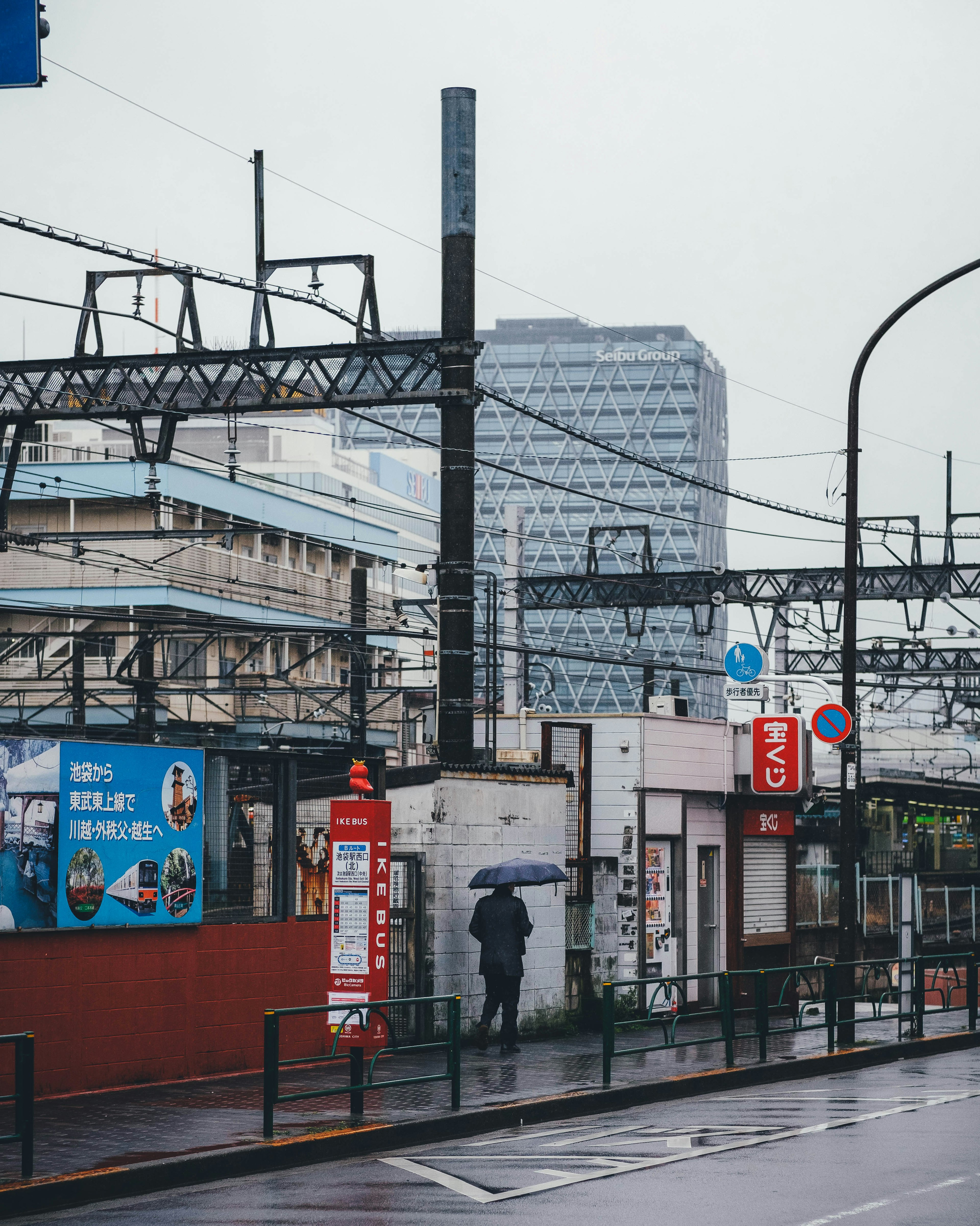 雨の中で傘を持った人が駅の近くを歩いている都市の景色