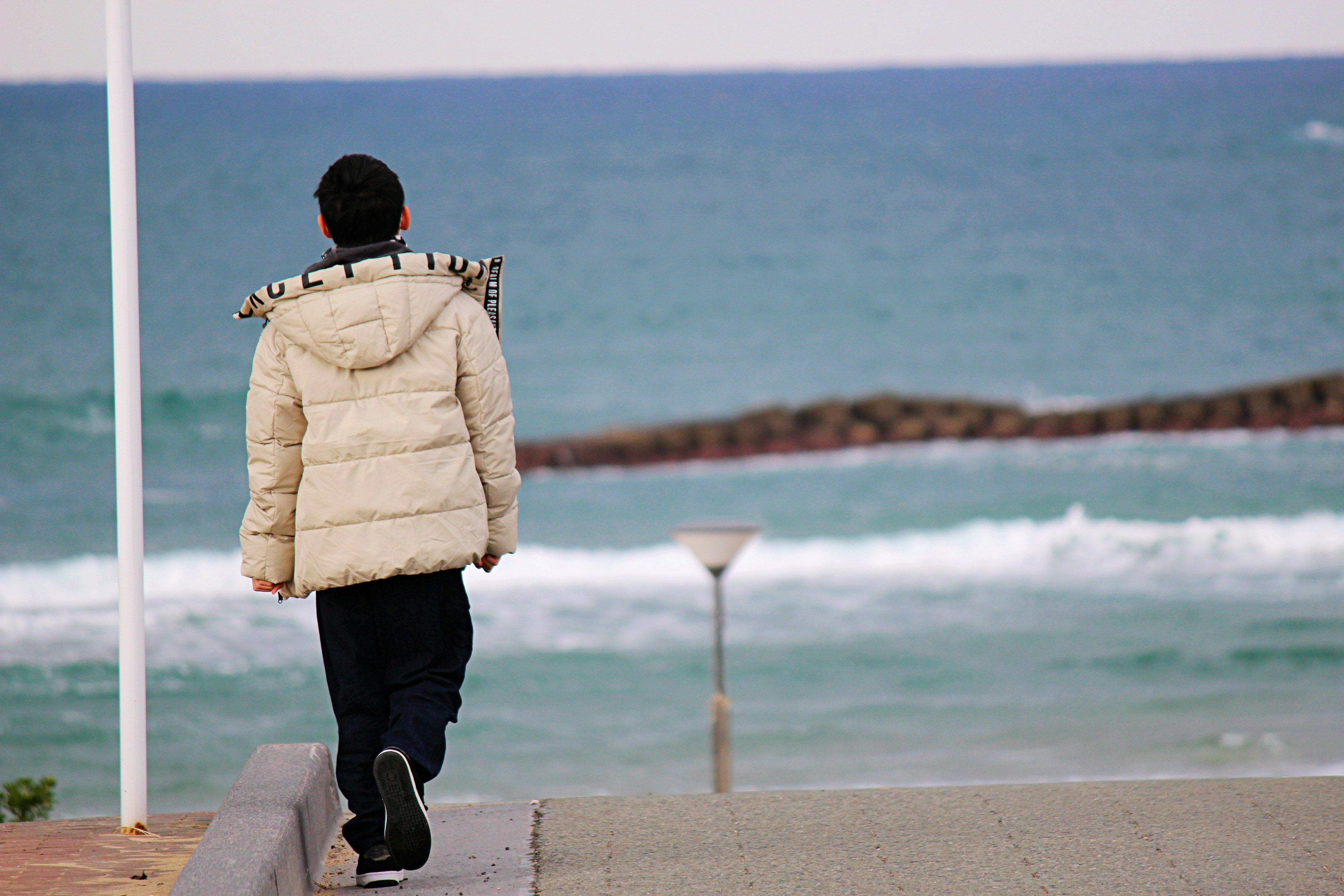 Persona caminando junto al mar con chaqueta blanca y pantalones negros