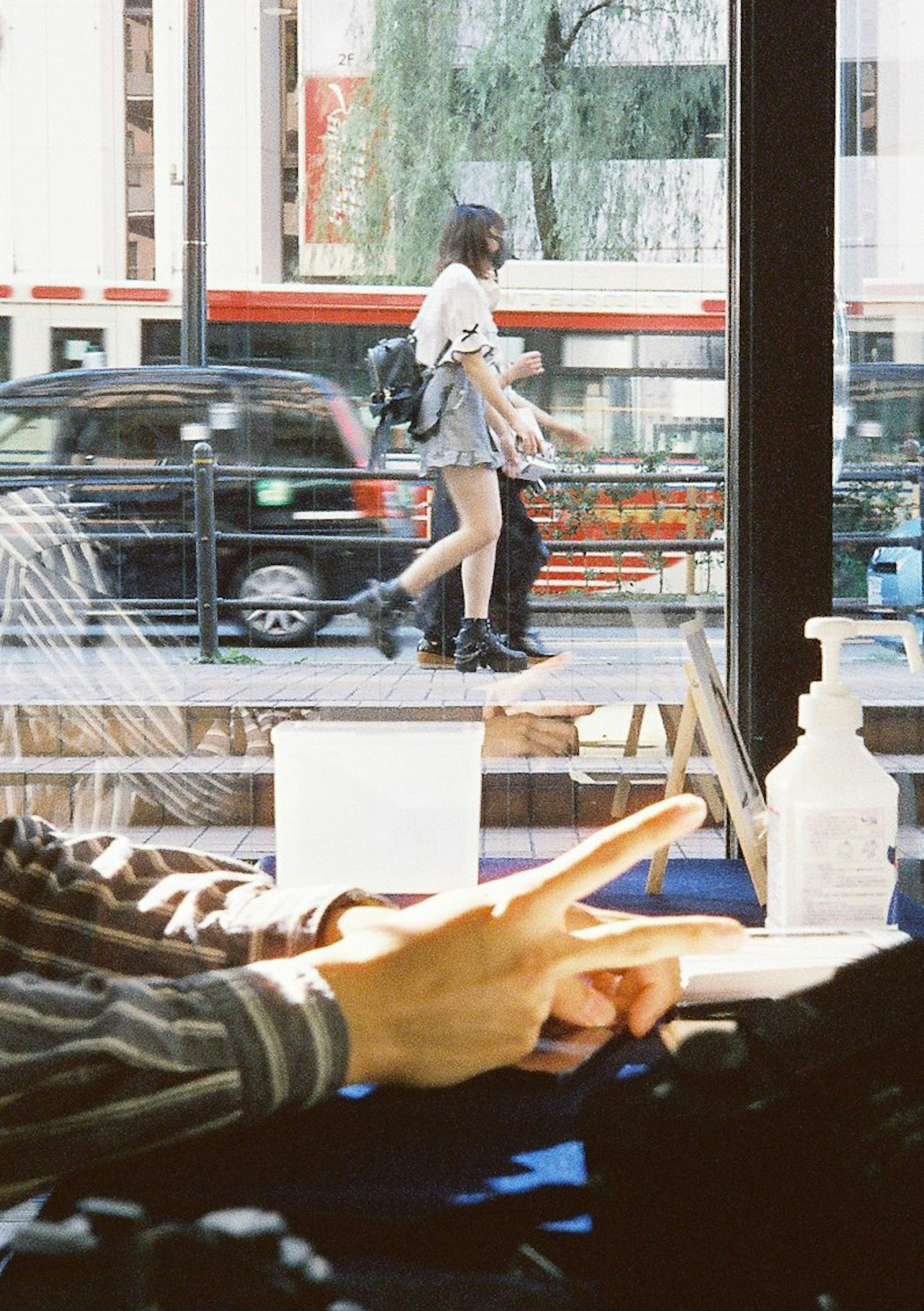 Manos descansando sobre una mesa con vista de una mujer caminando afuera de un café