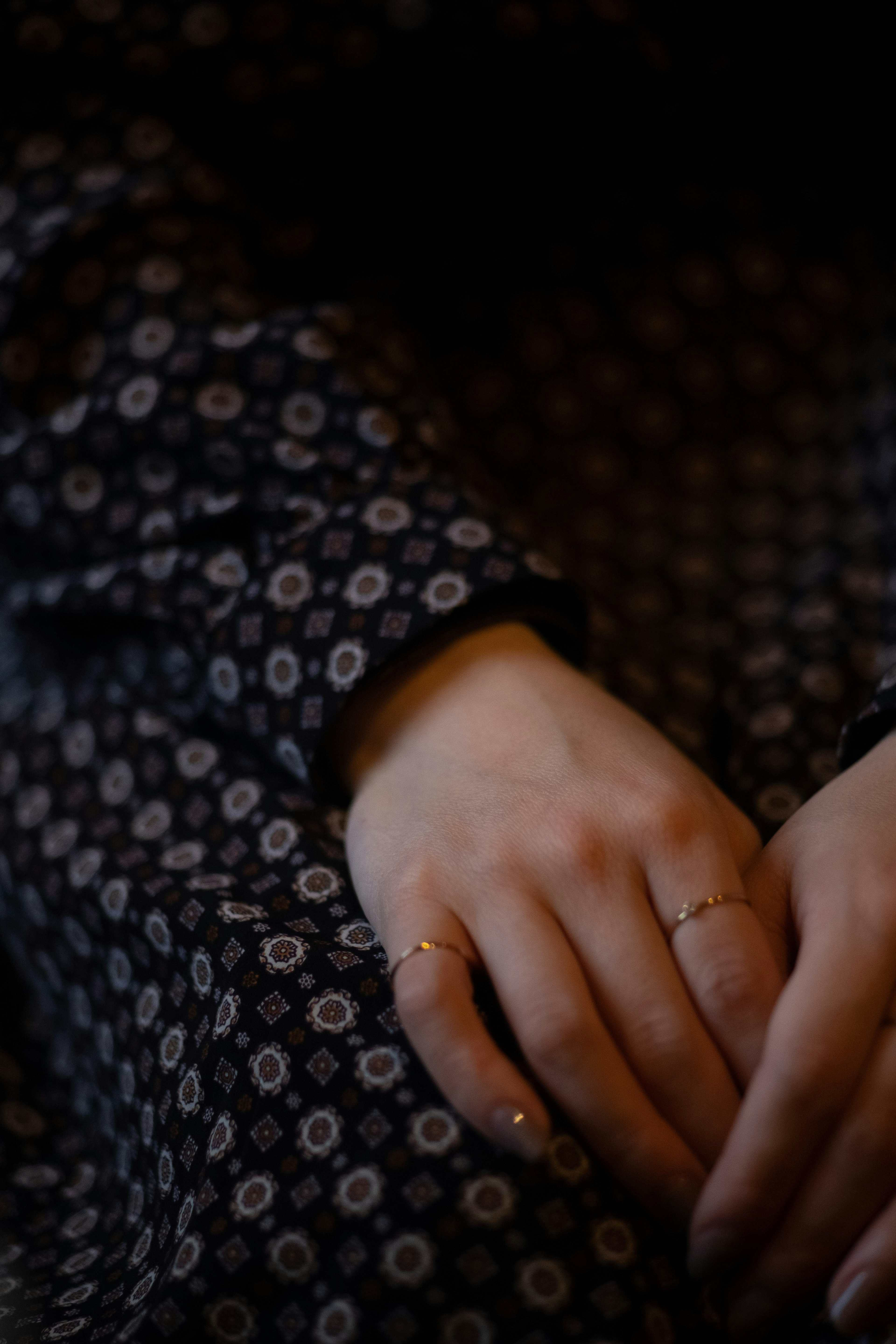 Hands adorned with delicate rings resting on a black floral patterned dress