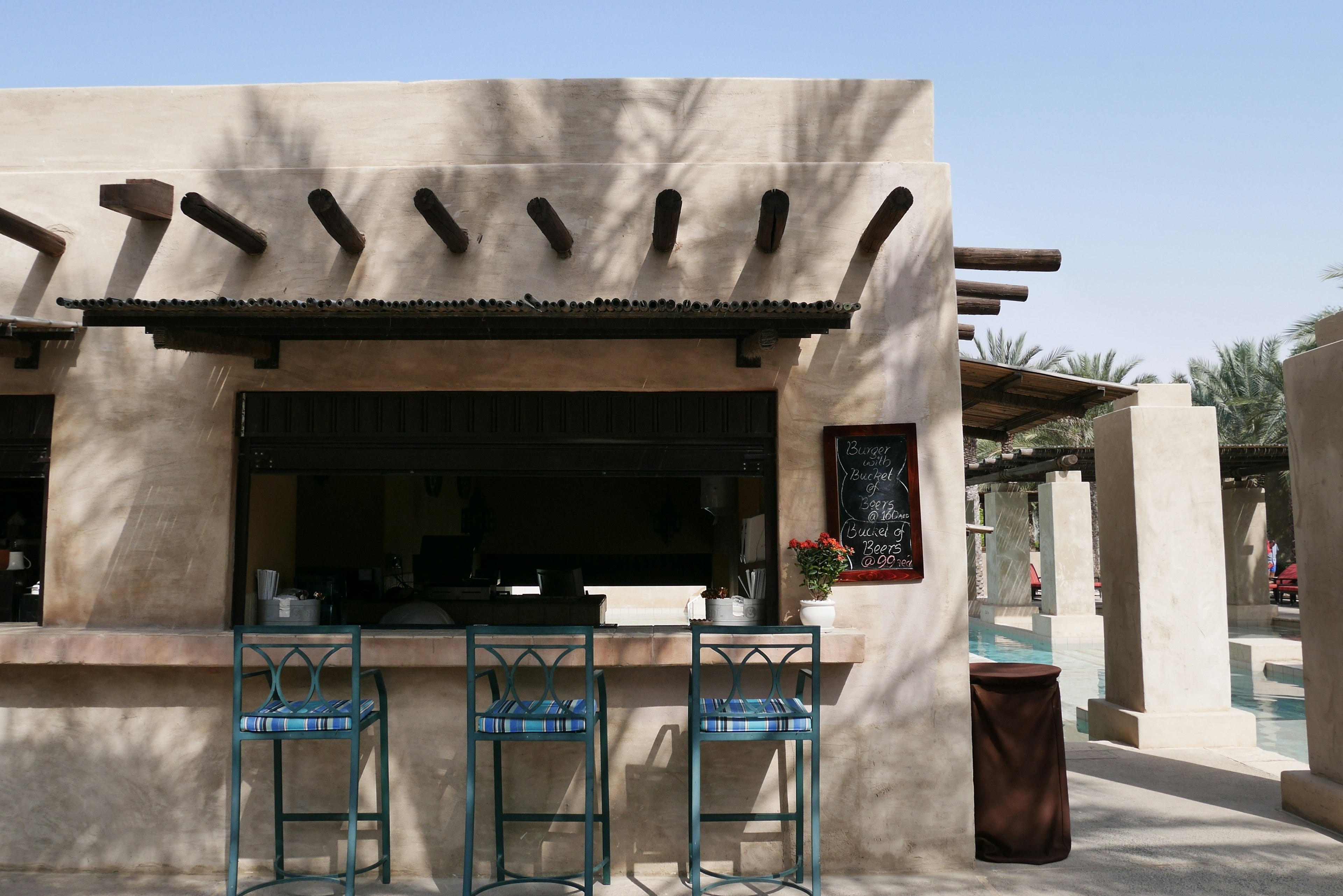 Exterior de café con paredes arenosas y vigas de madera con taburetes y un menú