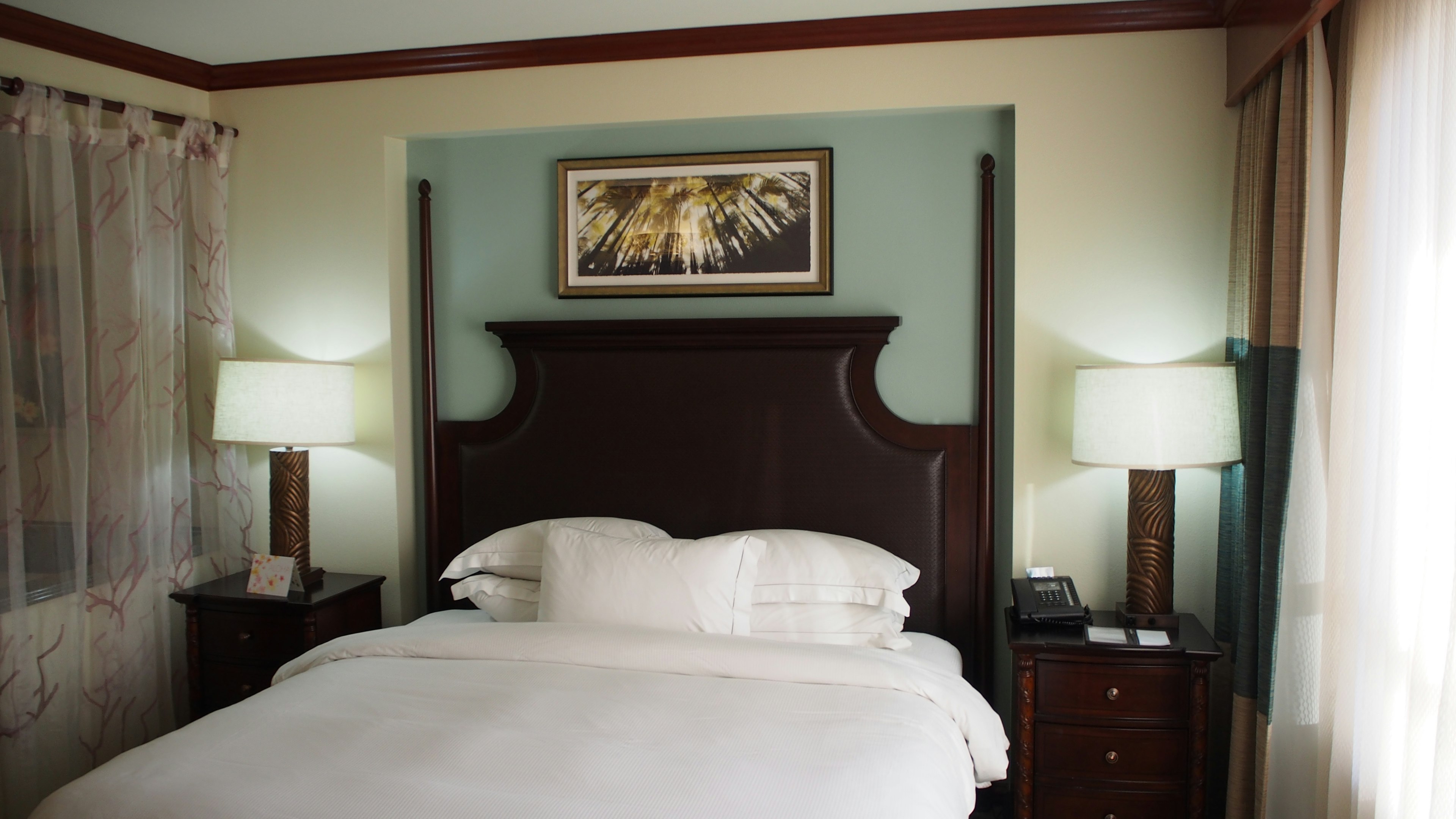 Cozy bedroom with wooden headboard, light blue wall, framed artwork, and soft natural light