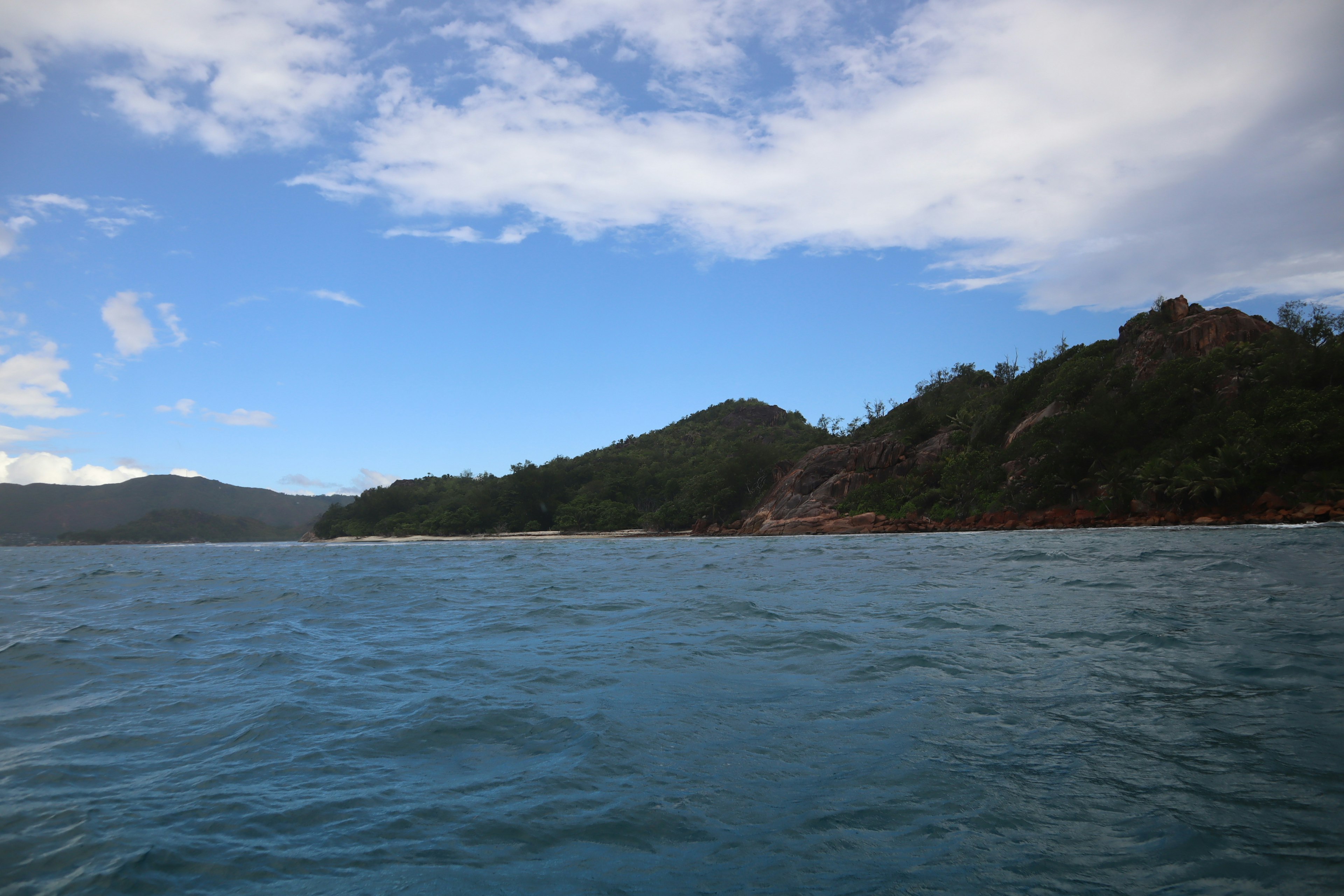 Pemandangan laut biru di bawah langit biru cerah dengan bukit di latar belakang