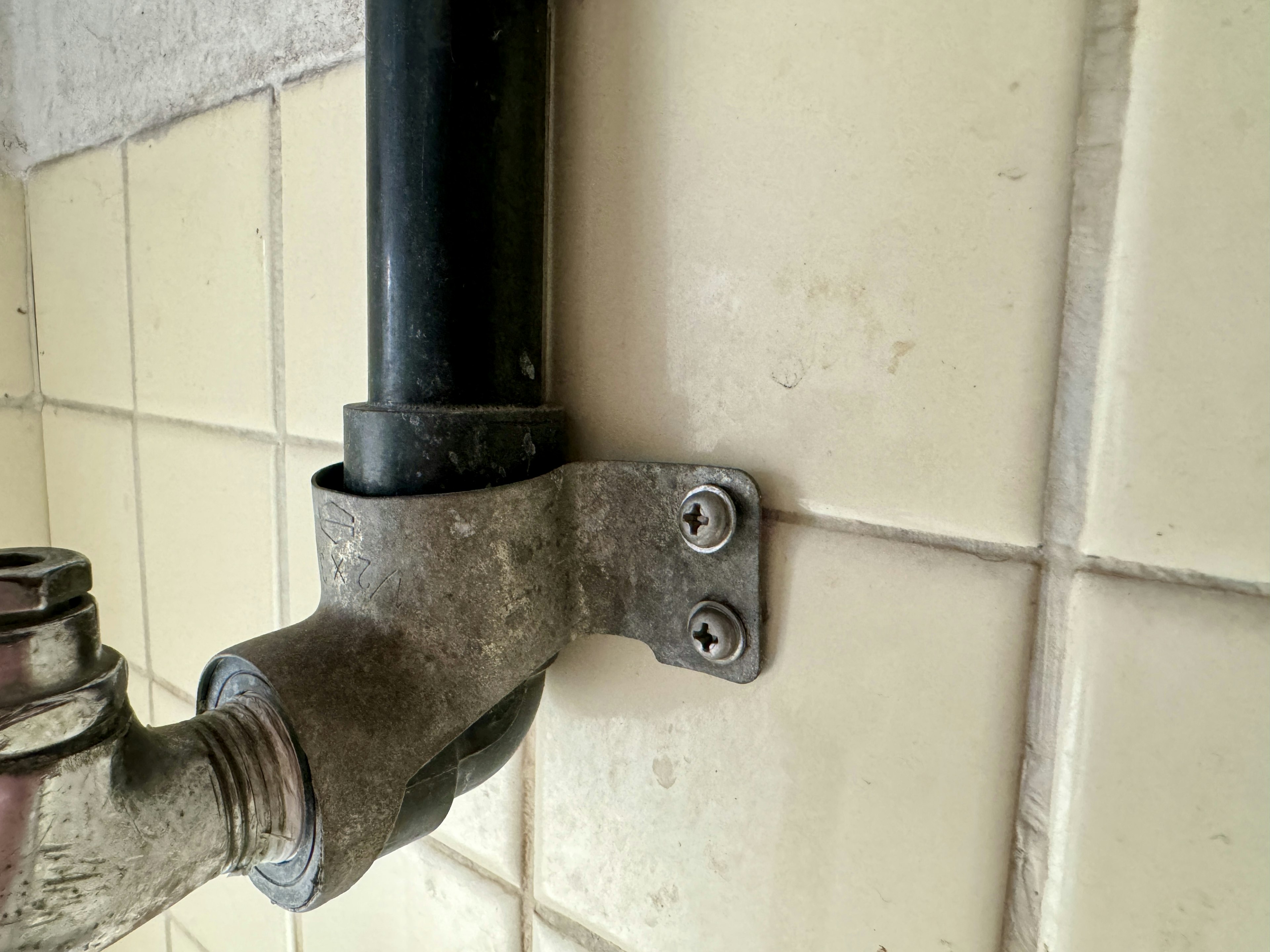 Metal connector with a black pipe attached to a tiled wall