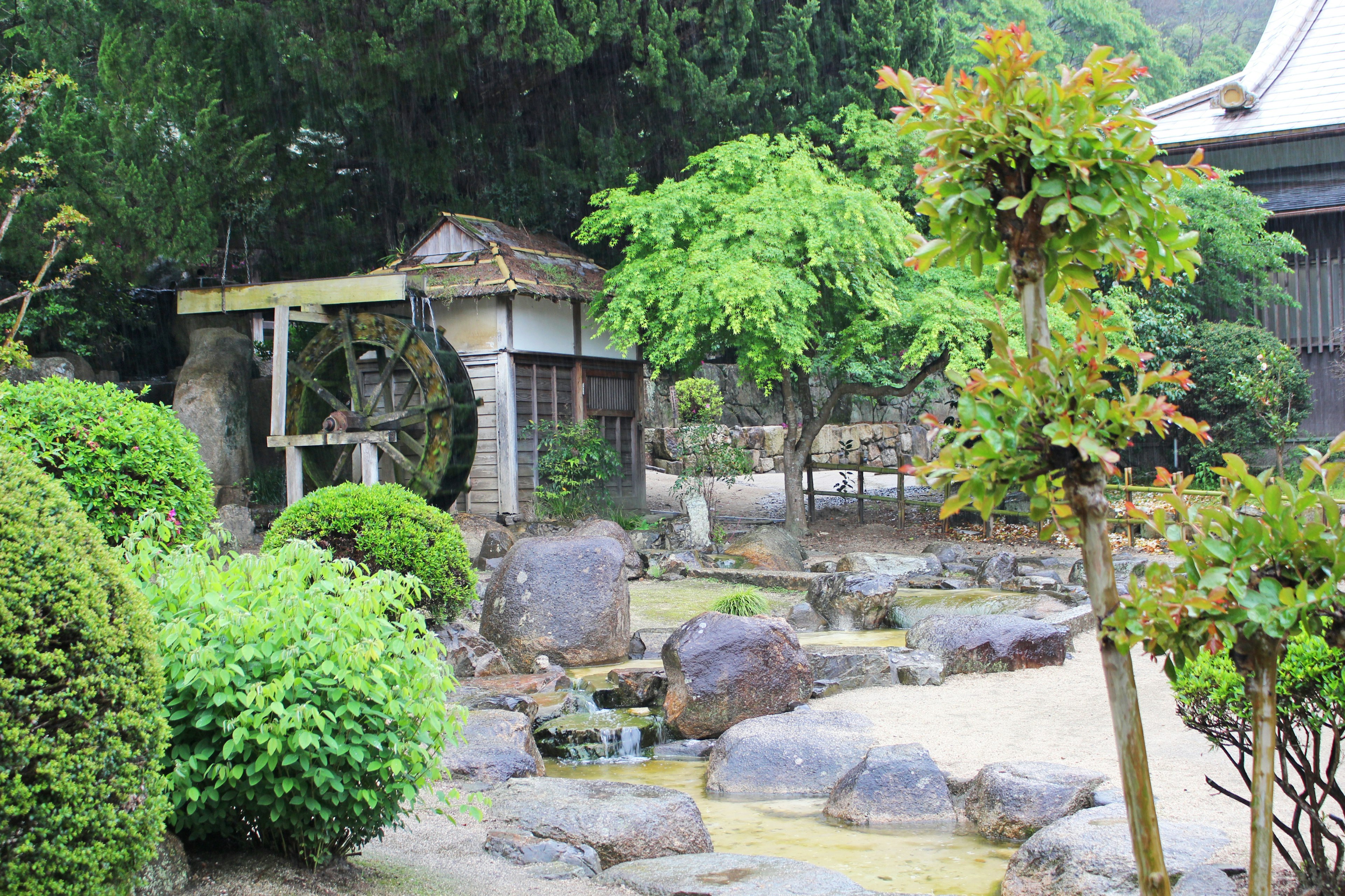 Bella scena di giardino giapponese con una ruota idraulica e vegetazione lussureggiante, rocce e acqua che scorre