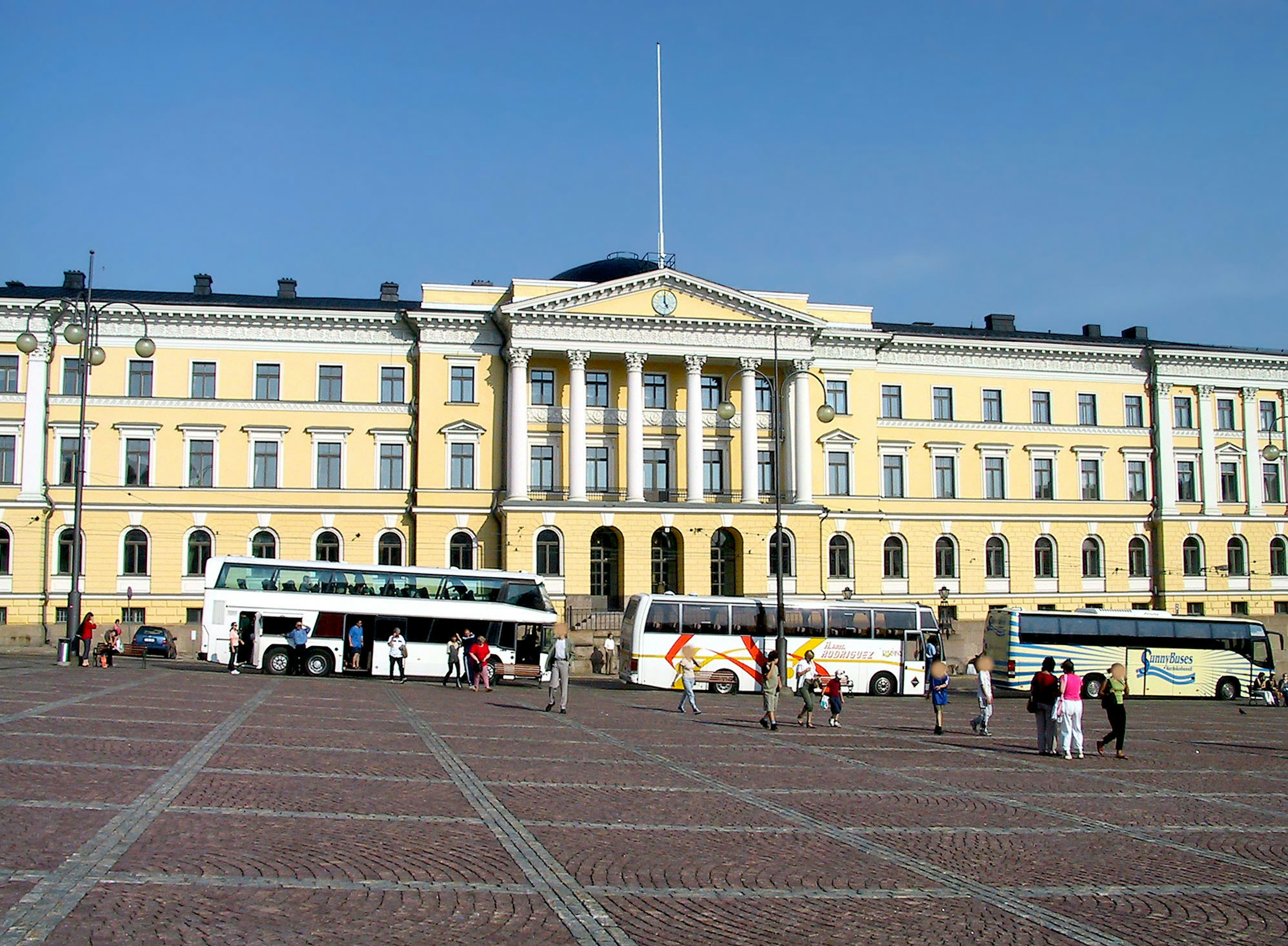 Grande edificio giallo a Helsinki con autobus parcheggiati nella piazza