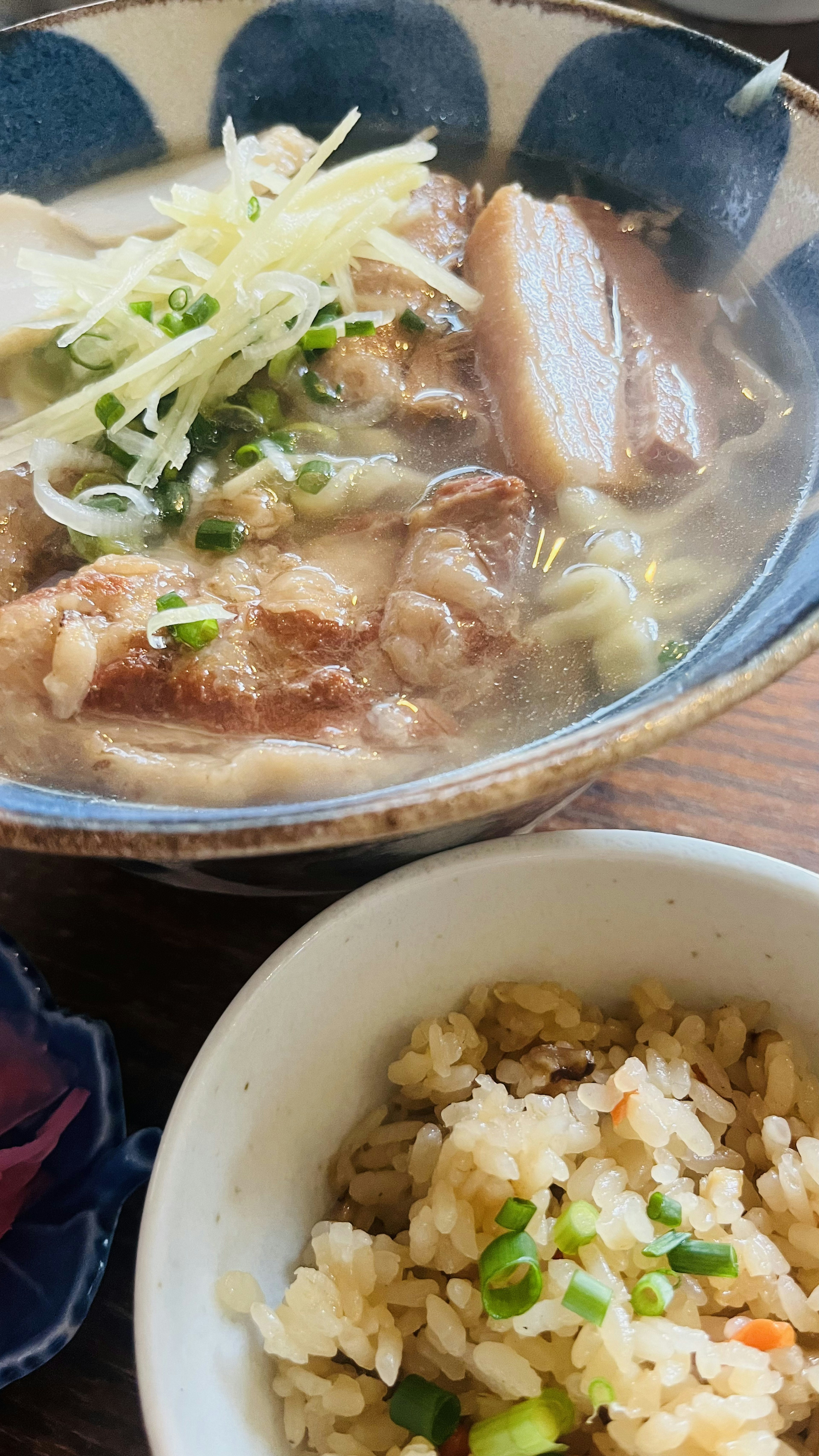 A bowl of steaming ramen with sliced pork and green onions alongside a bowl of fried rice