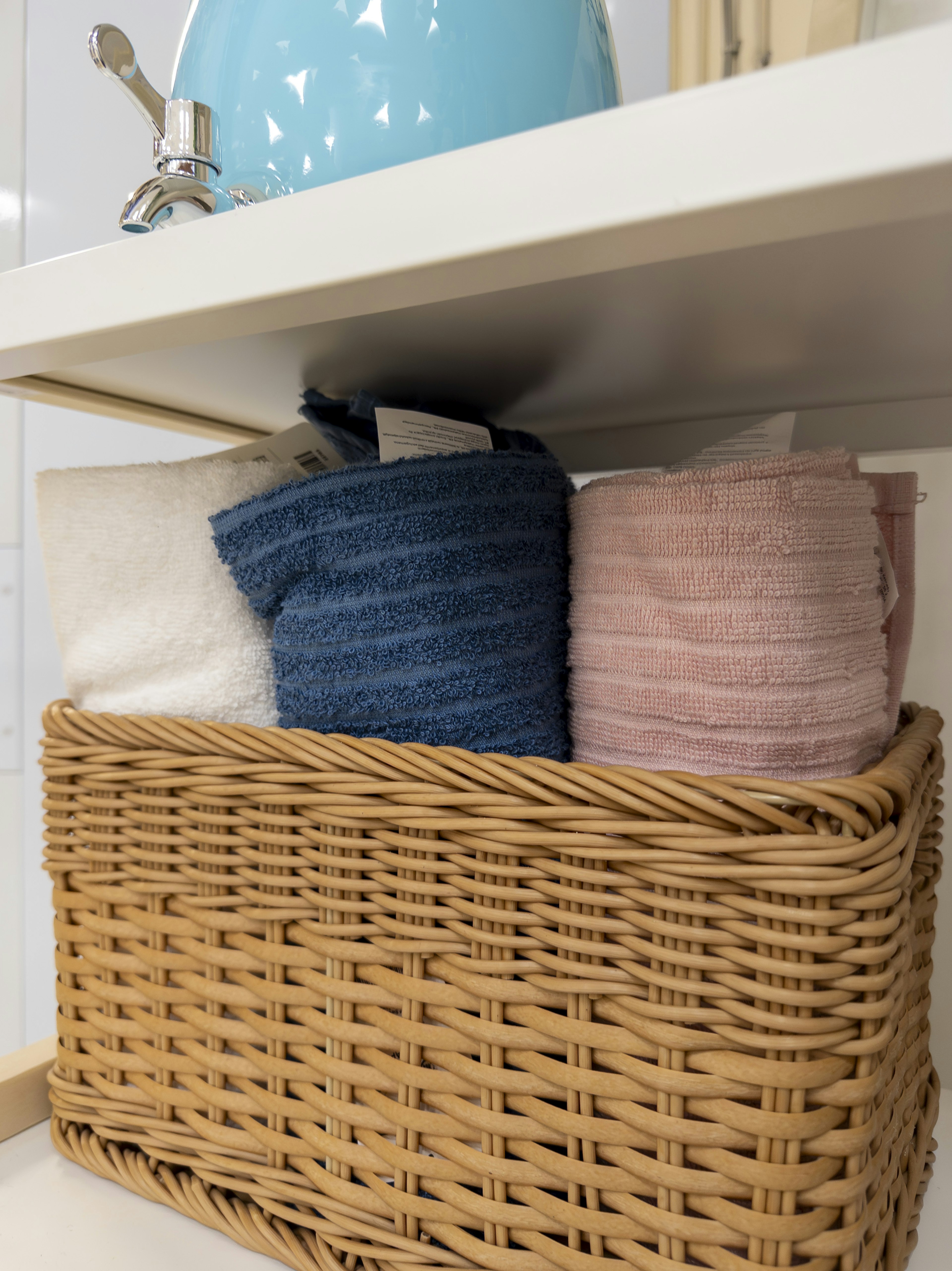 Towels stacked in a woven basket on a shelf with a blue faucet above