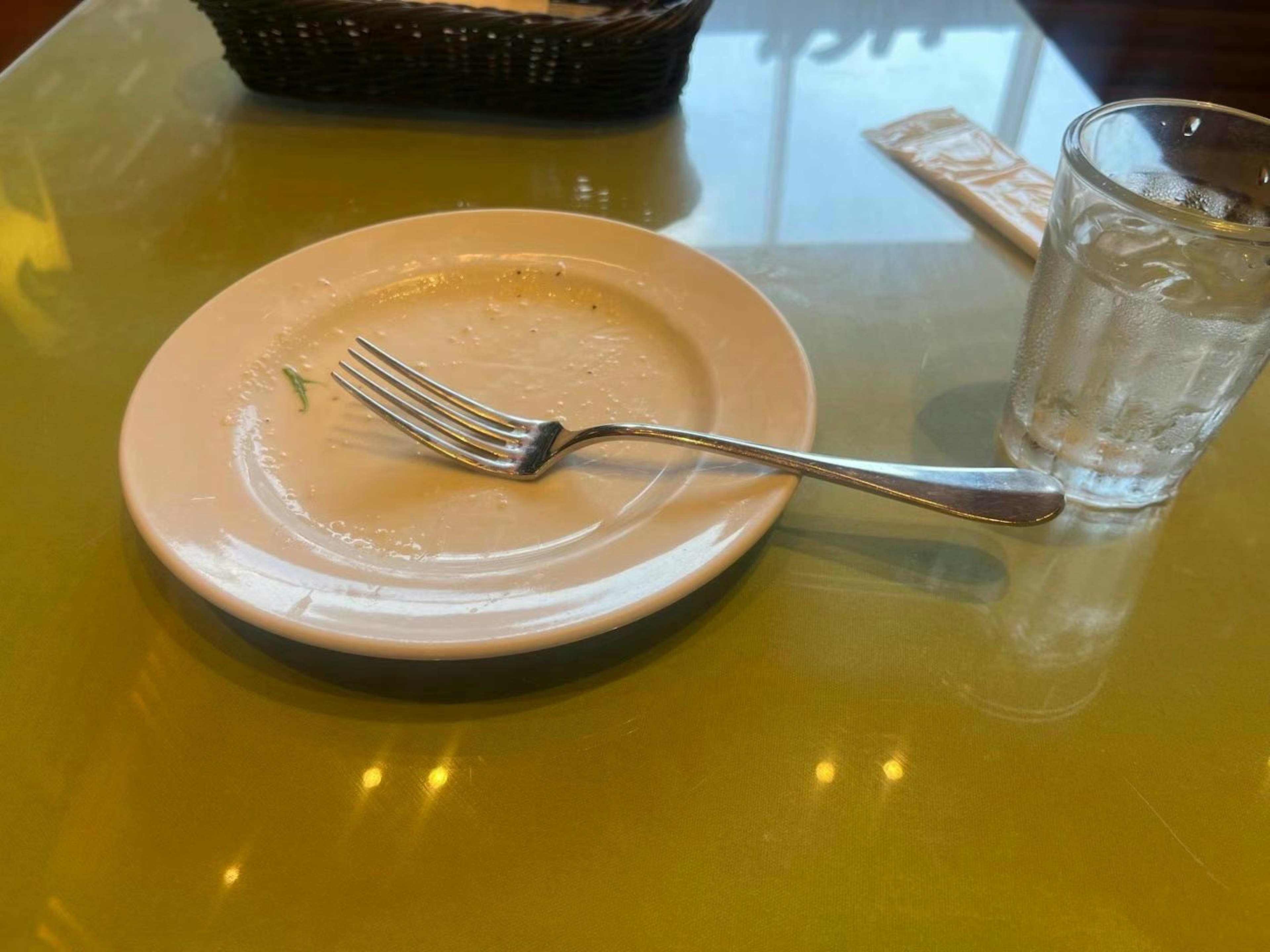 Un plato inacabado con un tenedor sobre una mesa transparente