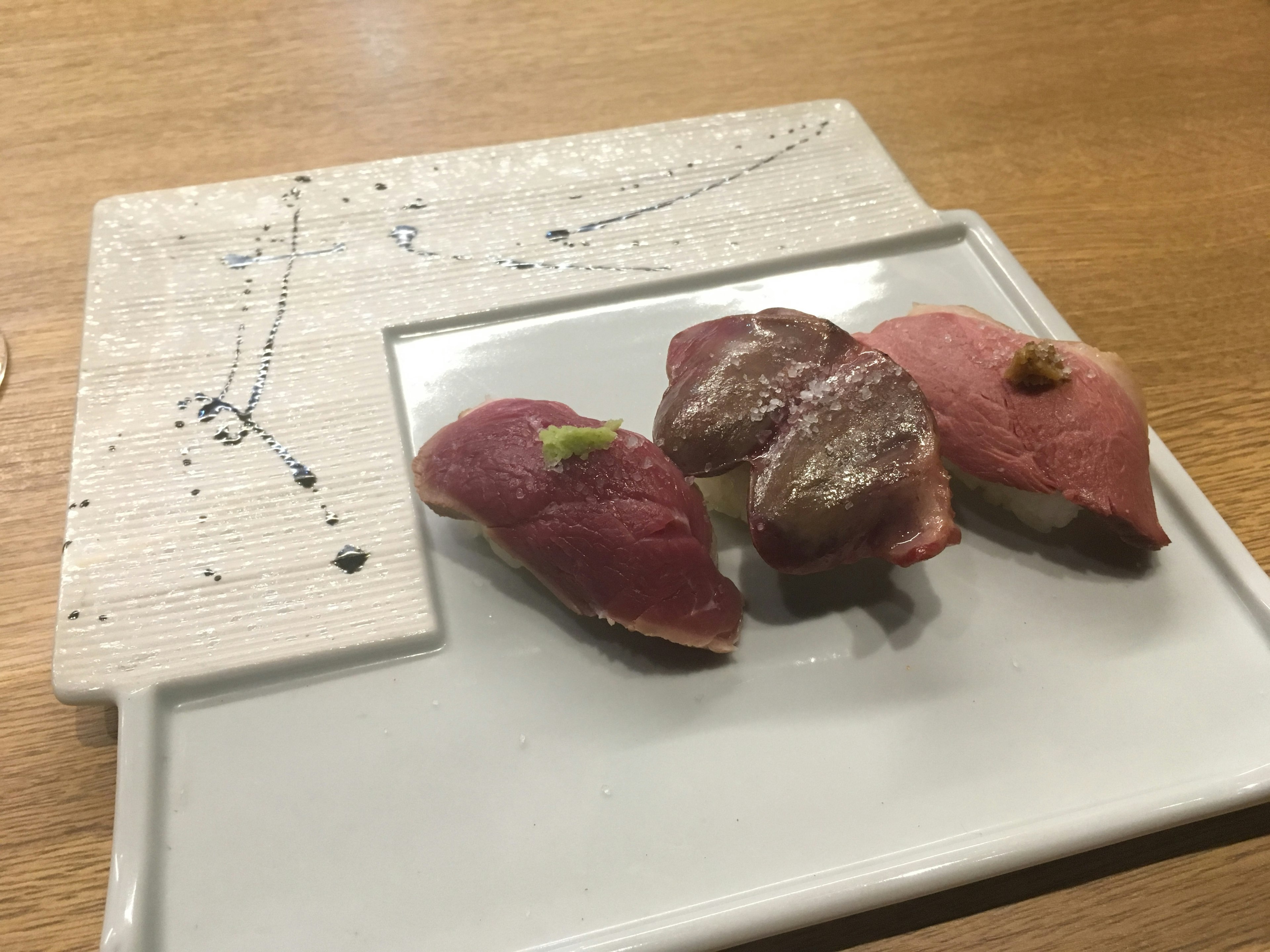 Three pieces of sushi arranged on a decorative plate featuring different colors and textures of fresh fish