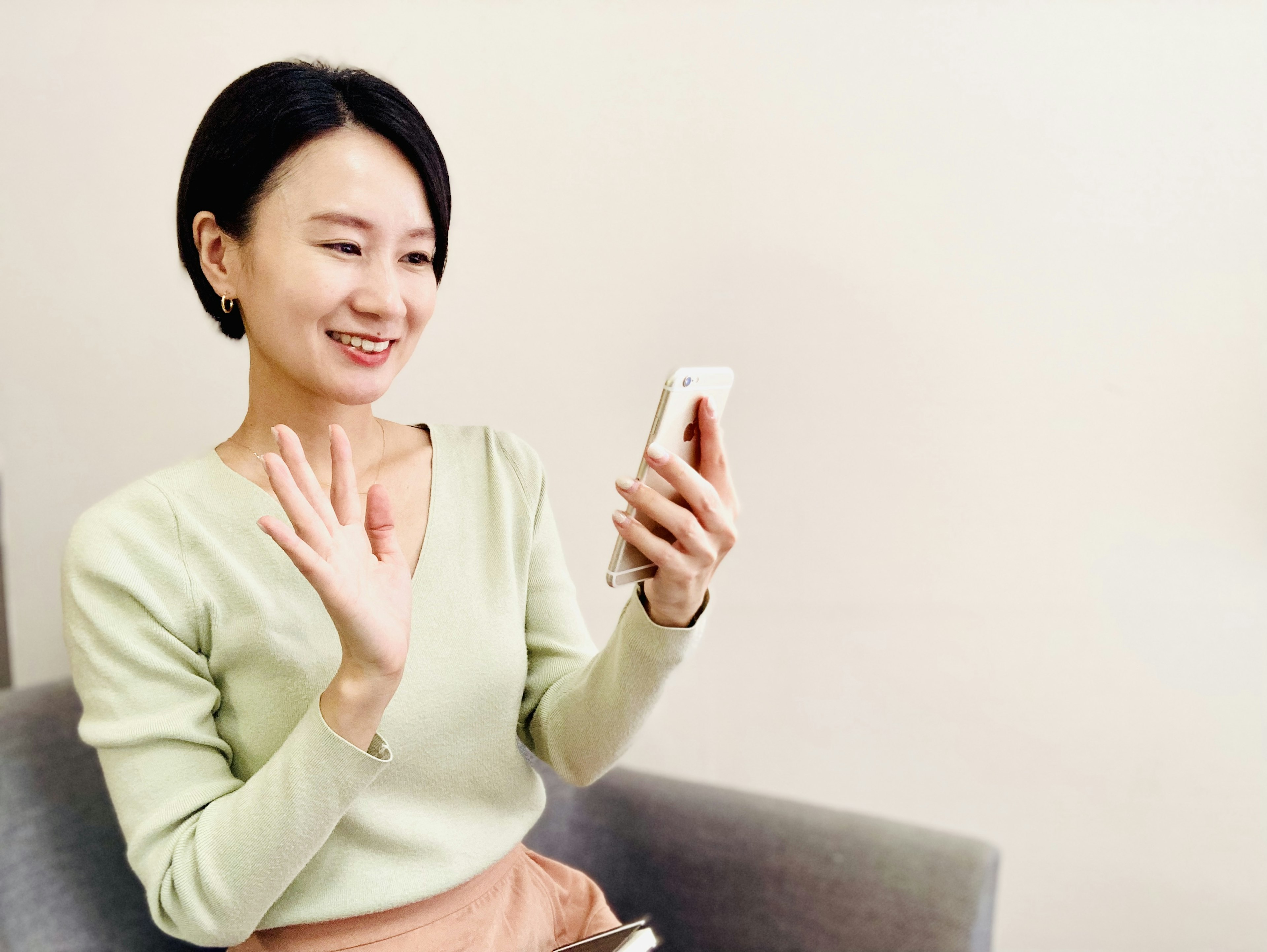 Una mujer con suéter verde sonriendo y saludando a su smartphone