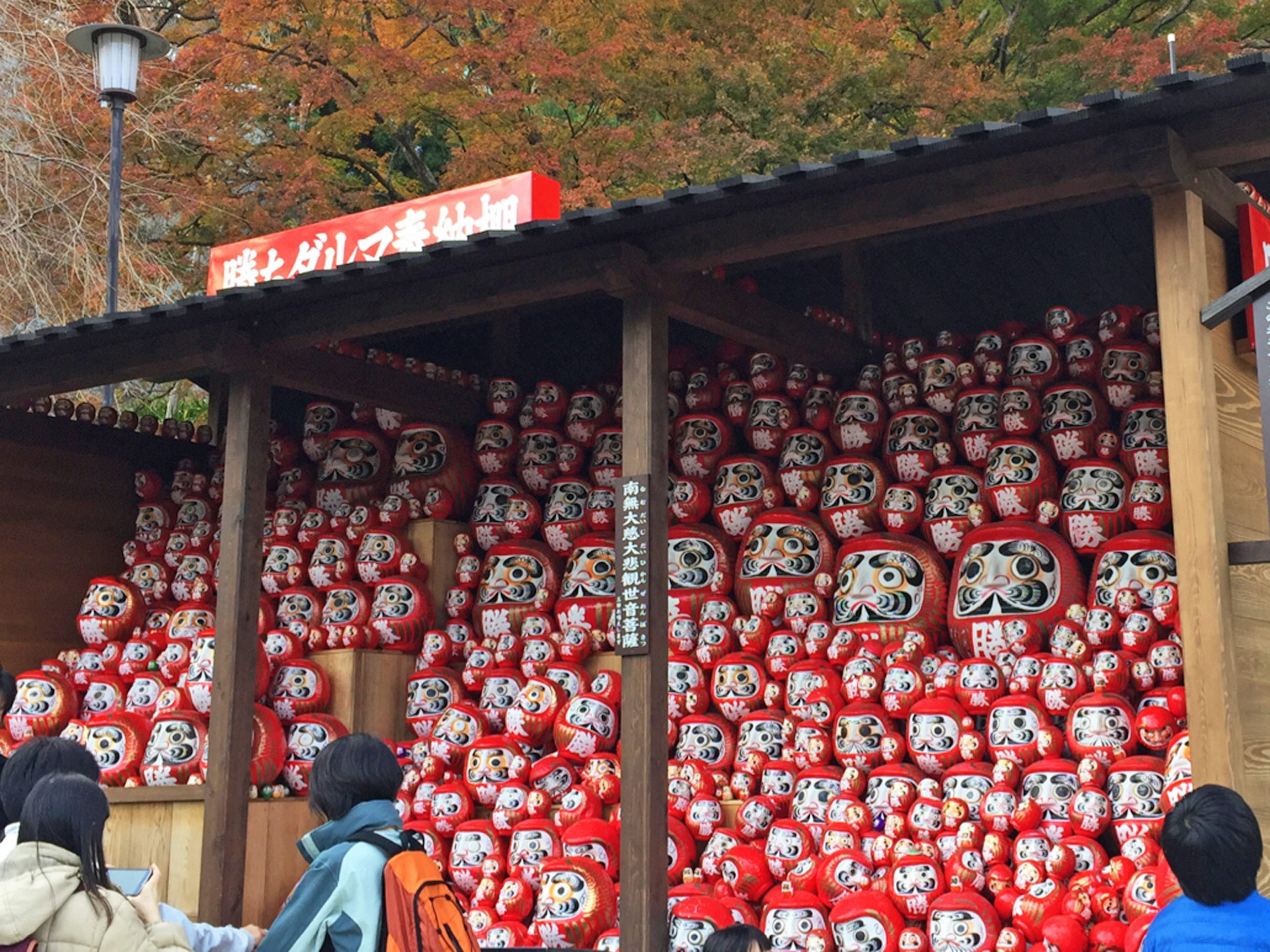 Una bancarella piena di numerose bambole Daruma rosse e persone