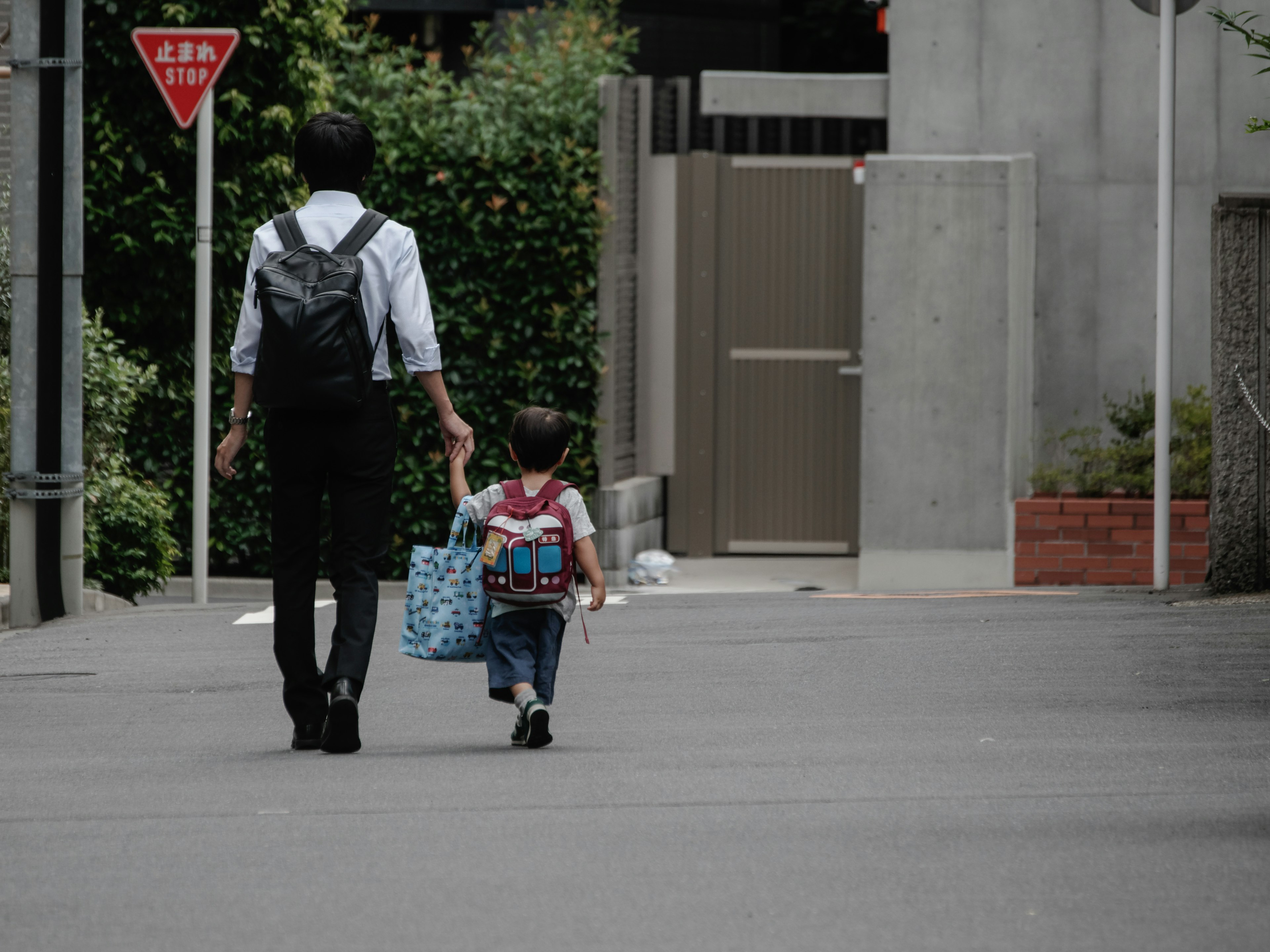 An adult and child walking together on a street surrounded by greenery and buildings