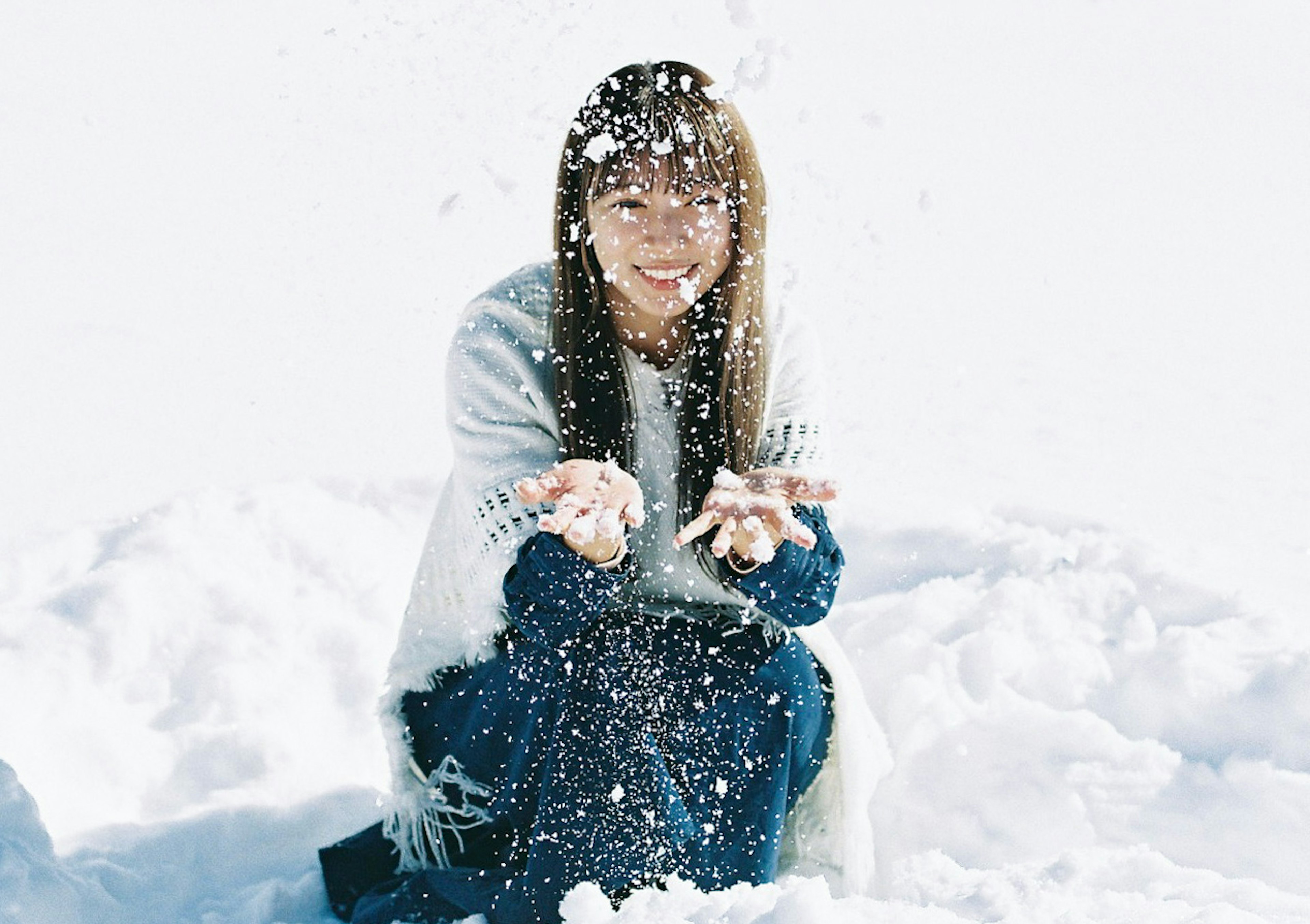 雪の中で笑顔で雪を持つ女性の写真